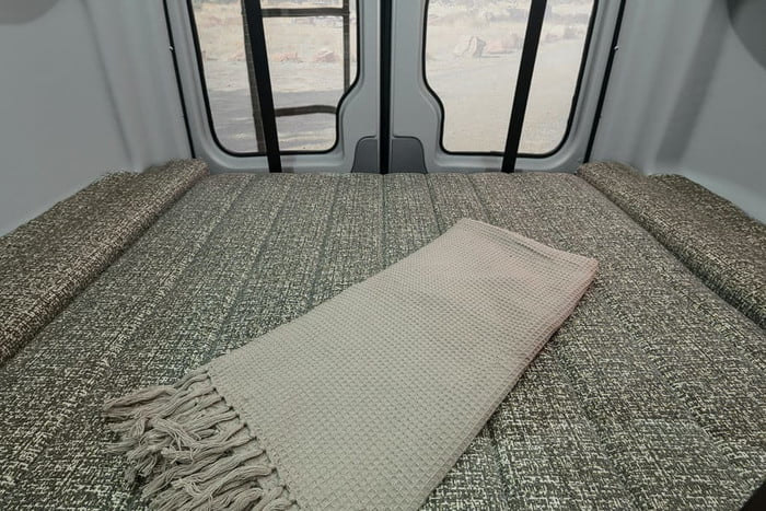 Experience an RV rental! This camper van's cozy bed, covered with a waffle-knit blanket, offers views from the rear doors.. Winnebago Revel 2020