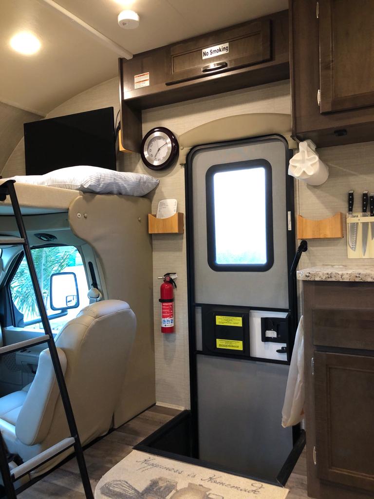 Explore this RV rental interior: cozy bunk, galley kitchen, entrance, and safety gear like a fire extinguisher.. Jayco Redhawk 2020