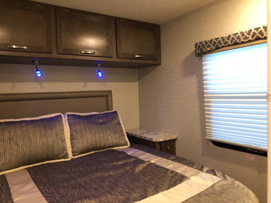 Spacious RV rental bedroom with a cozy bed, sleek overhead cabinets, and subtle blue accent lighting, designed for comfort on the road.. Jayco Redhawk 2020