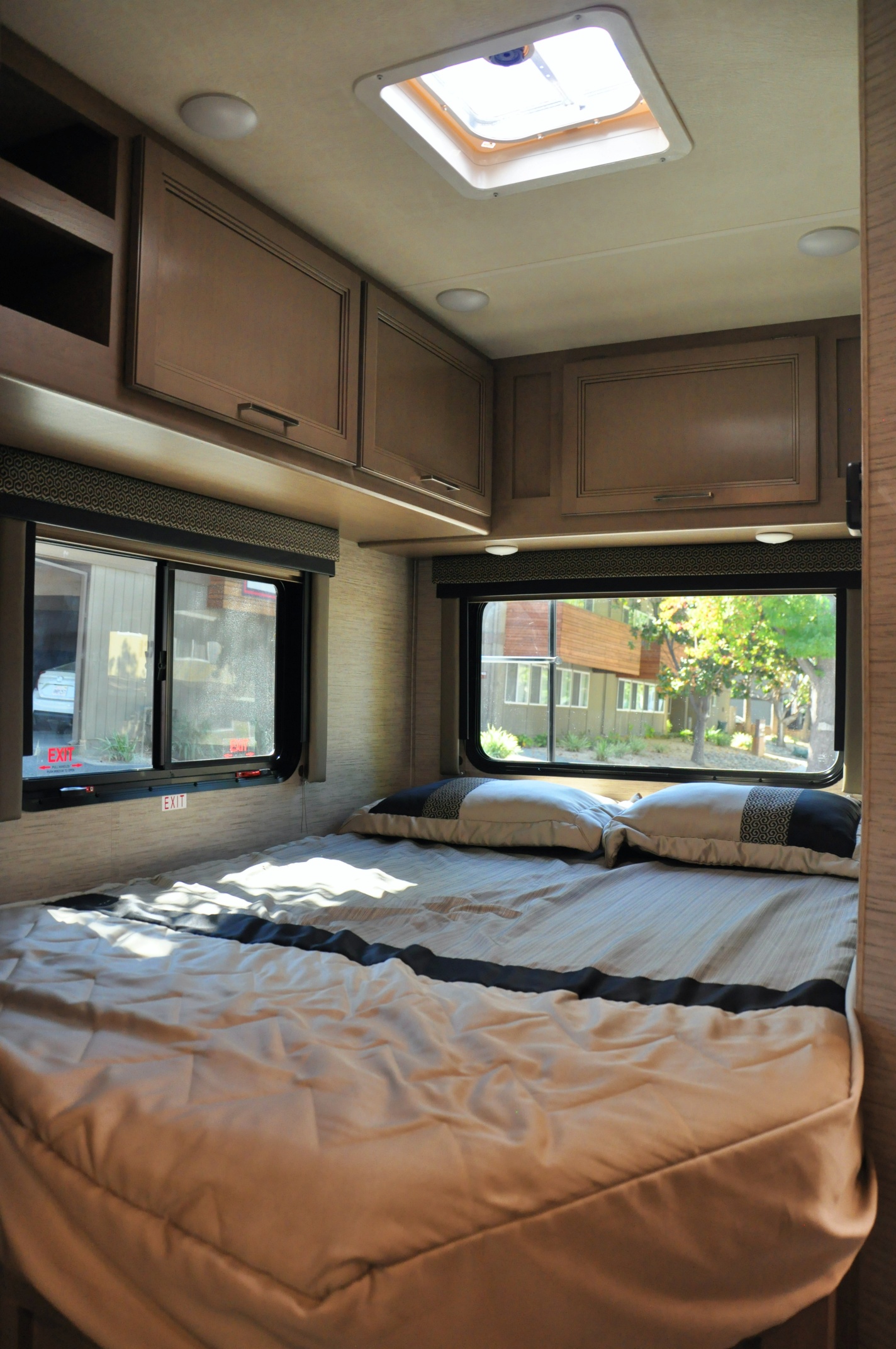 Inside a modern rv rental bedroom: a comfy bed, functional overhead cabinets, and bright windows with an outdoor view.. Thor Daybreak 2021