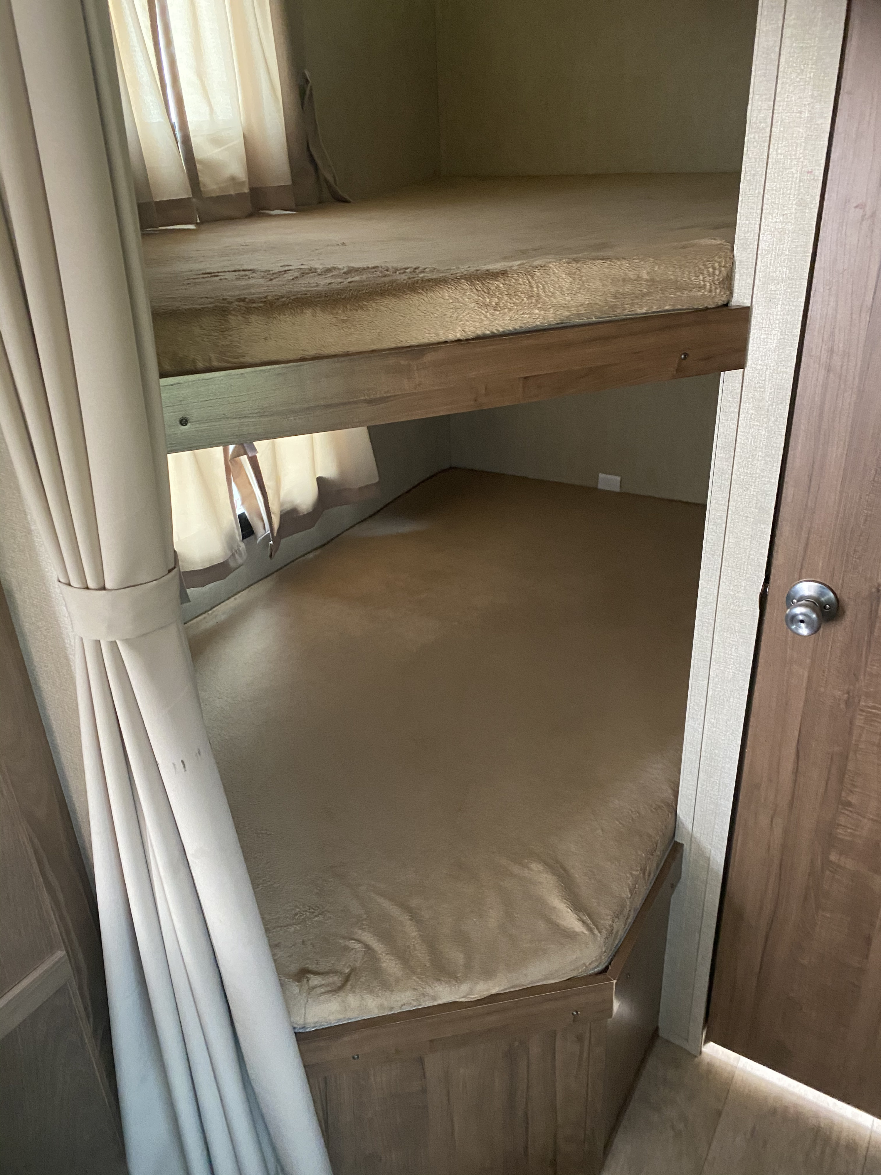 Inside an RV rental, this image displays two compact bunk beds with soft, tan covers and window curtains, ready for travel.. Gulf Stream Trailmaster 2018