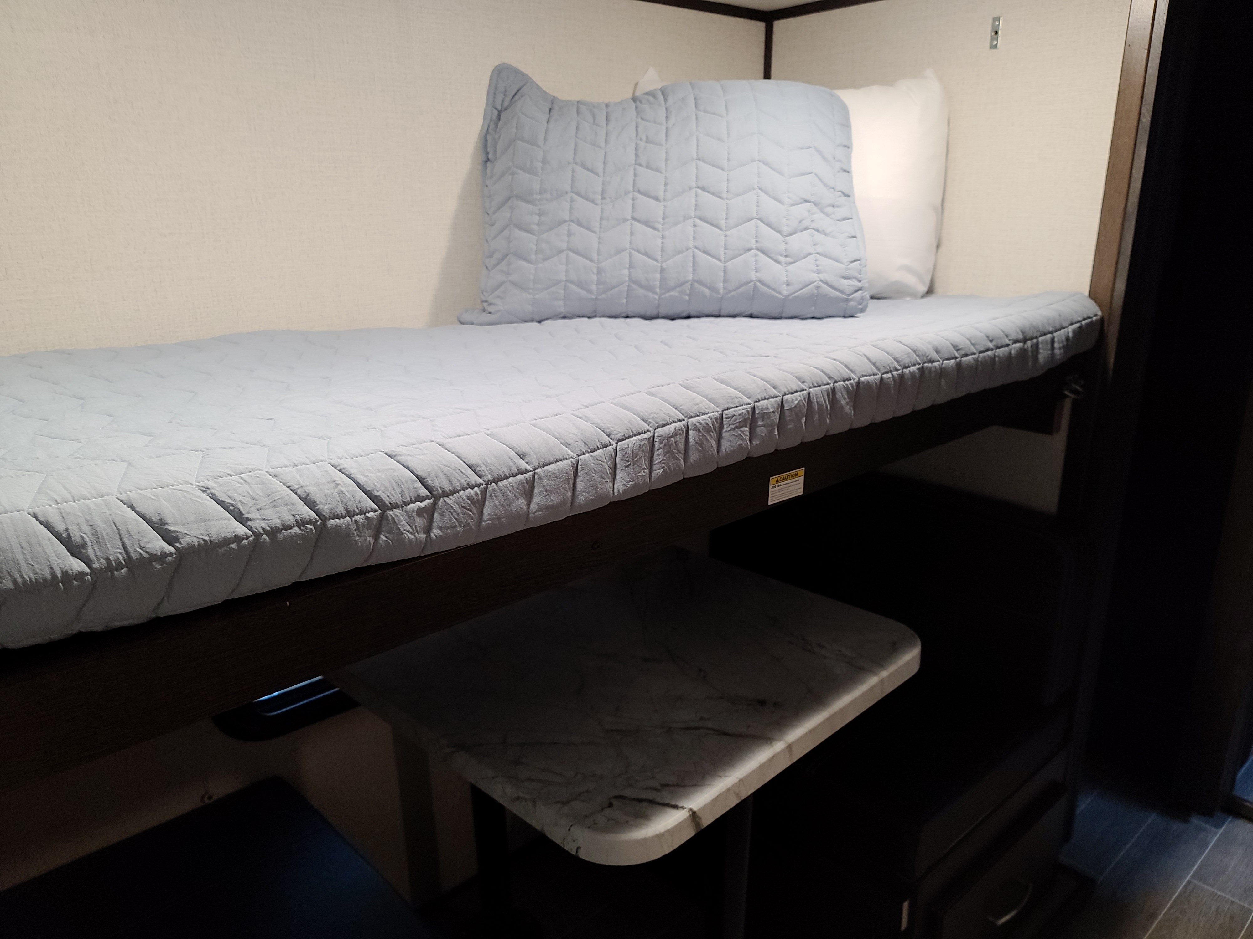 Discover this efficient RV rental bunk bed space, featuring quilted blue bedding, a pillow, and a handy lower table.. Dutchmen Other 2020