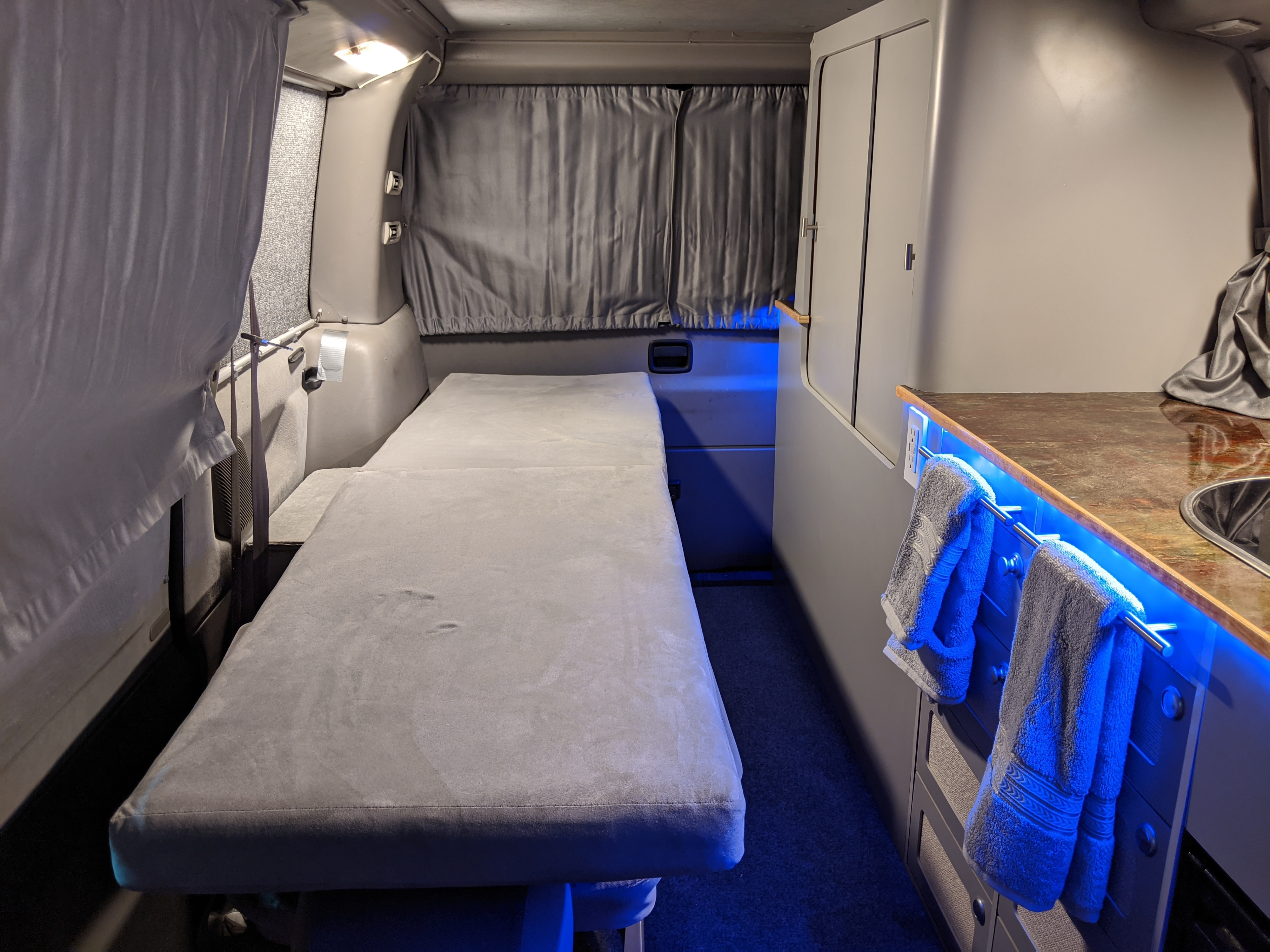 RV rental interior featuring a versatile bed, compact kitchen with sink, and cool blue LED lighting. Ideal for travel.. Volkswagen T4 Westfalia 2002