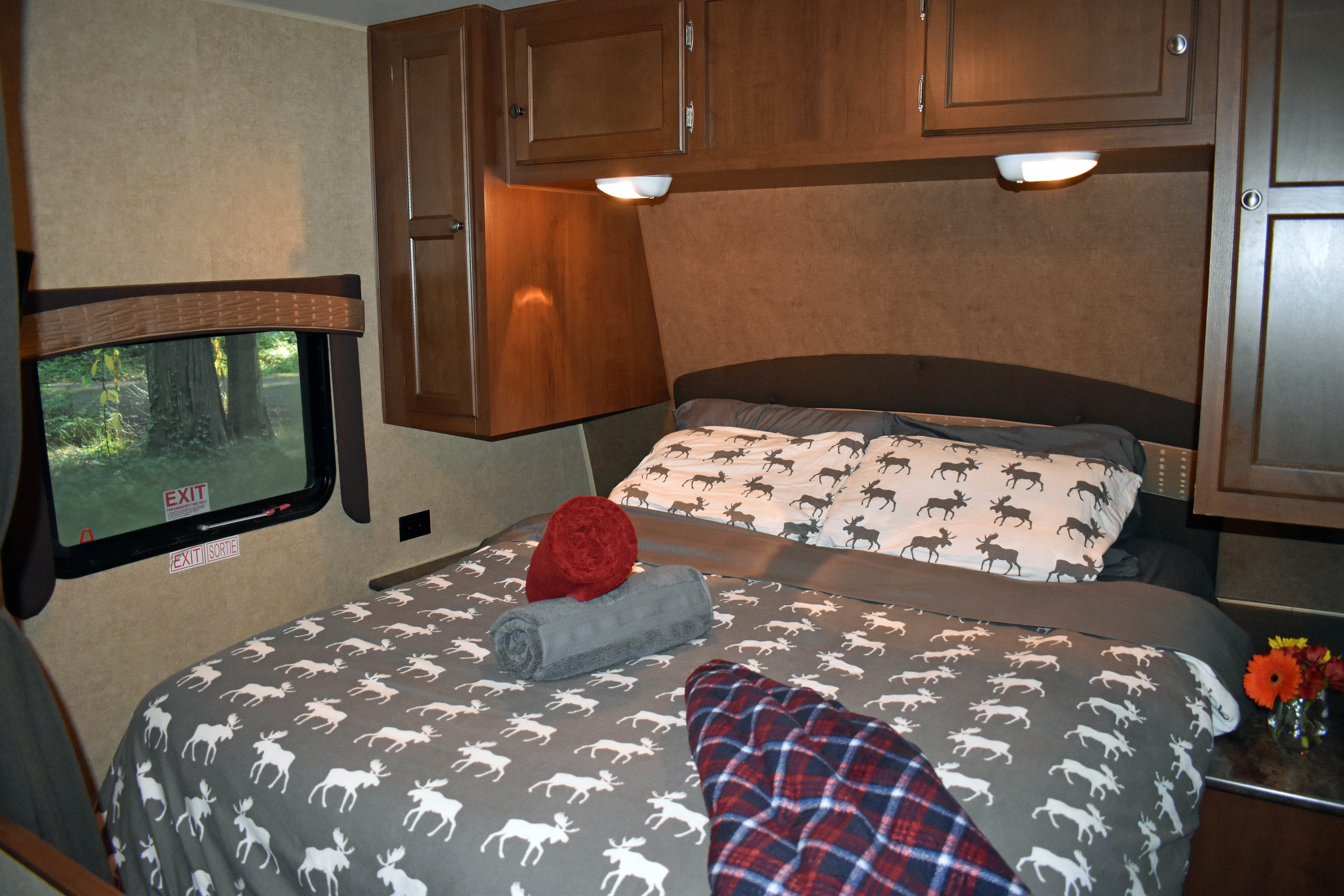 Inside a cozy **RV rental** bedroom. Features a comfortable bed with moose-patterned bedding, window, & functional cabinetry.. Jayco Jay Flight 2014