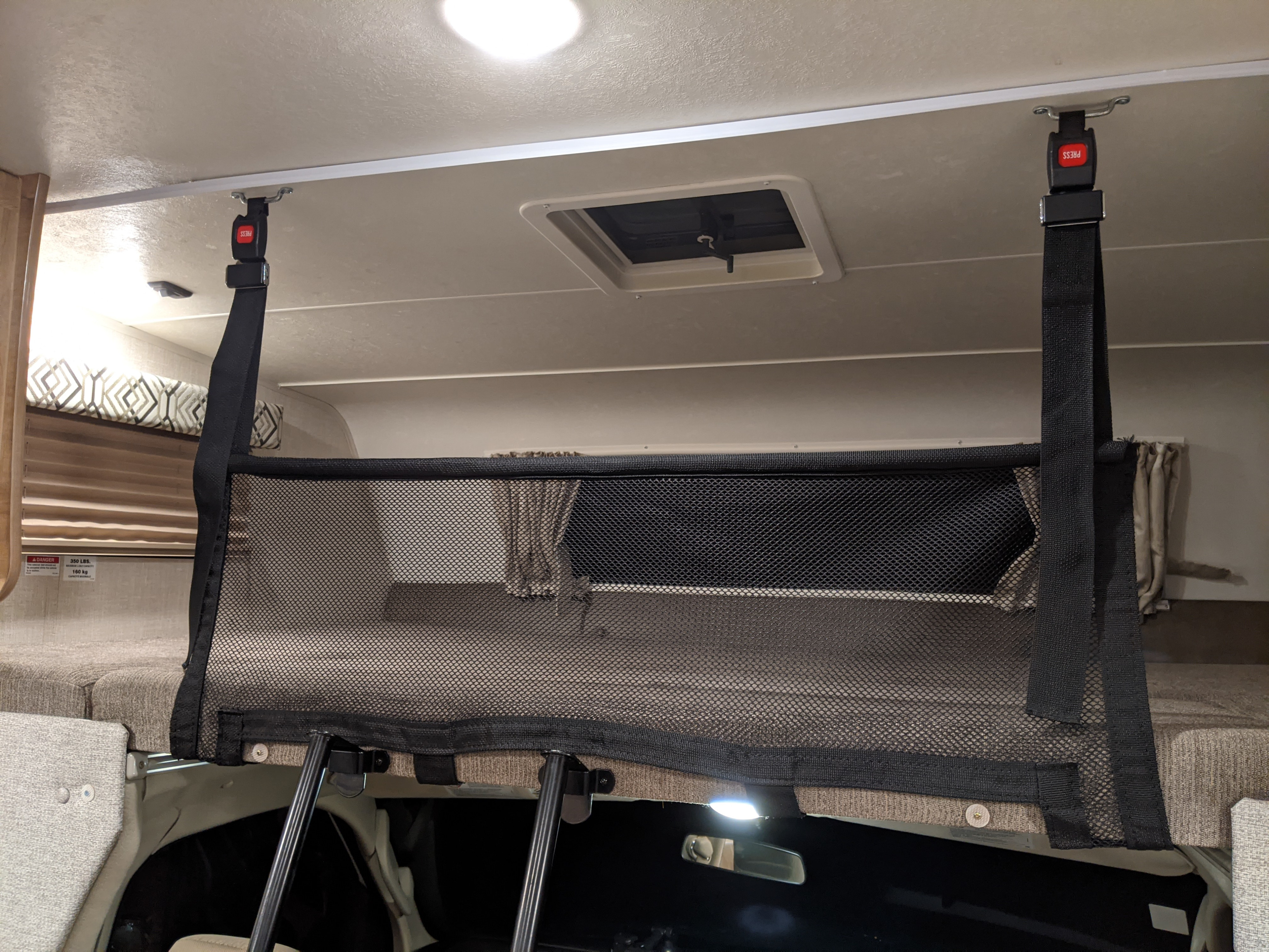 Inside an **rv rental**: a top bunk with a black mesh safety net, secured by ceiling straps, for safe overhead sleeping.. Leprechaun 230RB 2020
