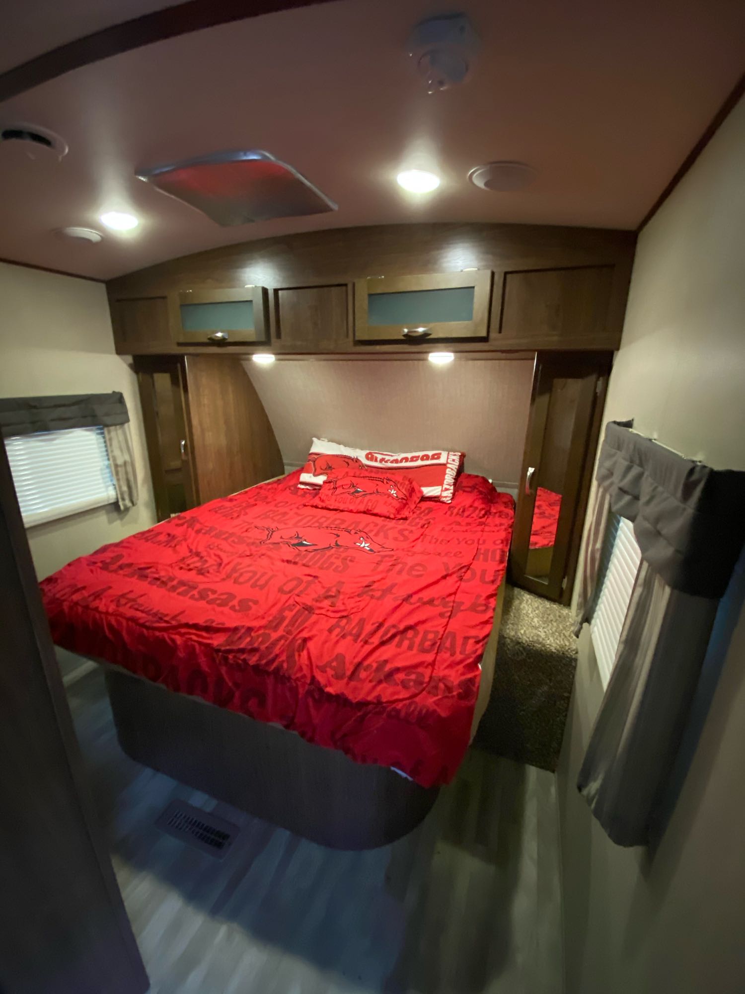 Cozy RV rental bedroom interior with red Arkansas Razorbacks bedding, overhead cabinets, and bright lights.. Dutchmen Aerolite 2017