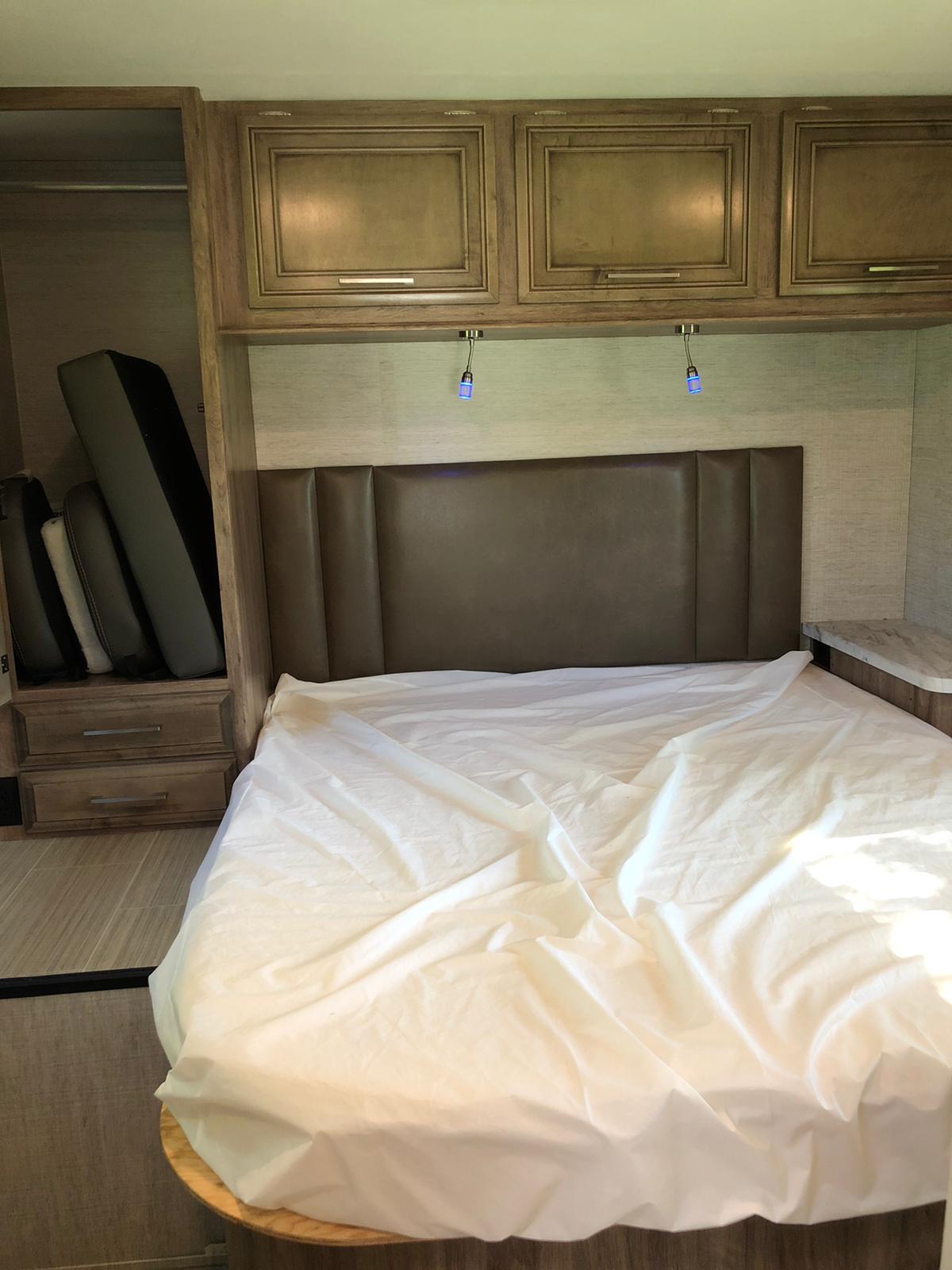 RV rental bedroom showing a bed with white sheets, headboard, overhead cabinets, and reading lights.. Entegra Coach Odyssey 29K 2021