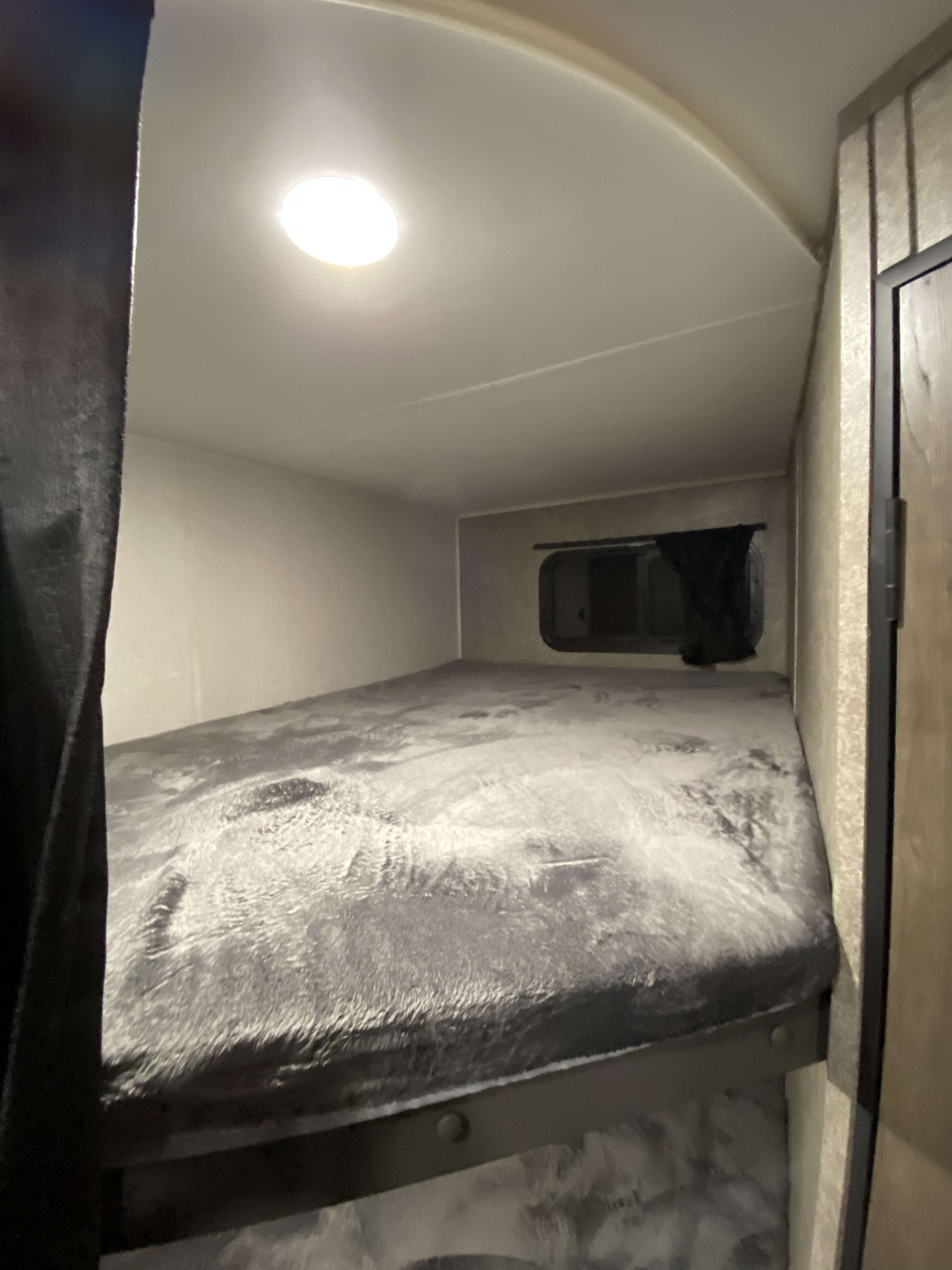 Cozy RV rental bunk bed, featuring a soft gray blanket and a small window with a dark curtain for privacy.. Open Range Open Range 2021