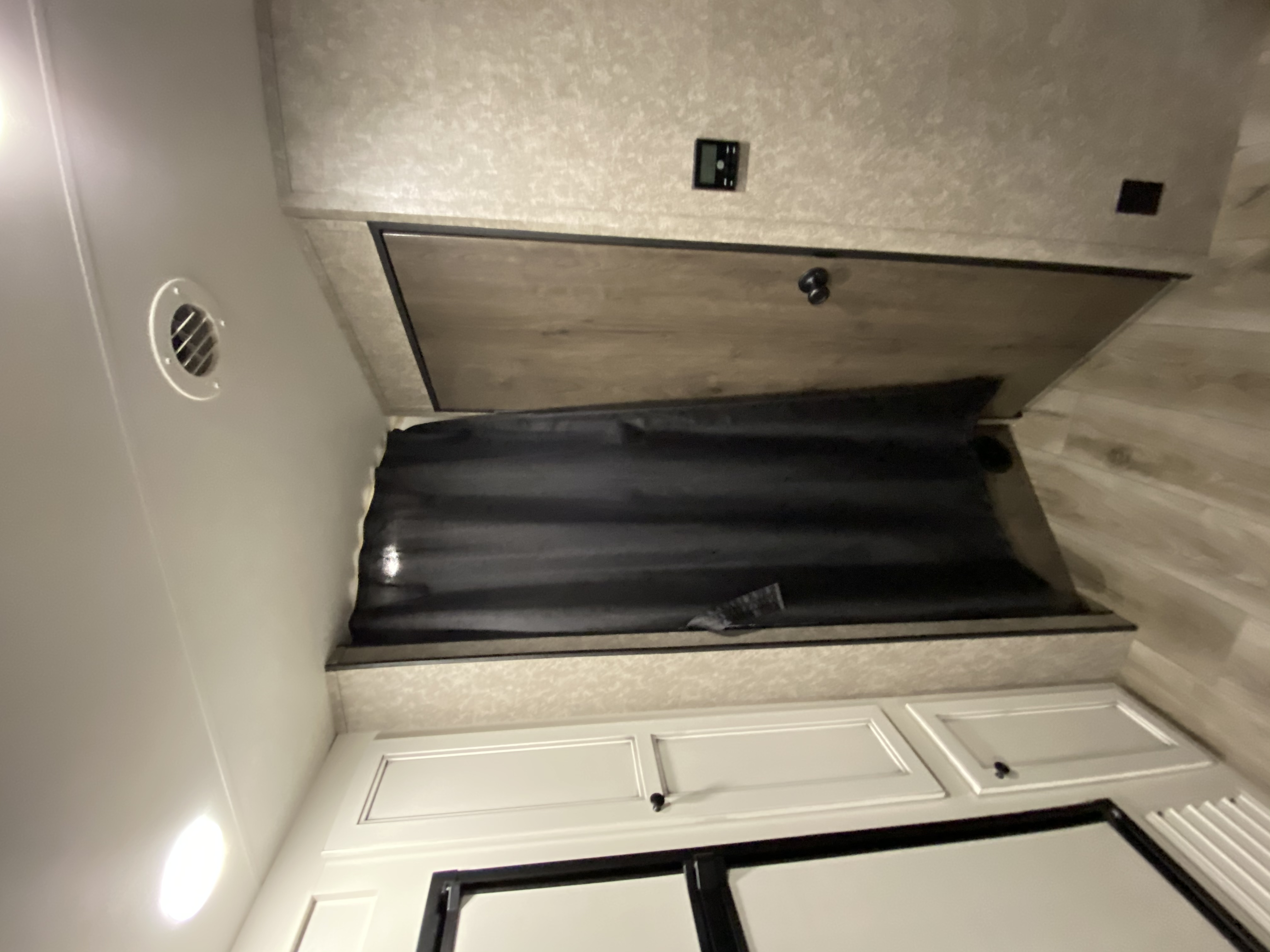 Inside an RV rental: a cozy bunk bed with a dark privacy curtain, overhead cabinets, and a vent.. Open Range Open Range 2021
