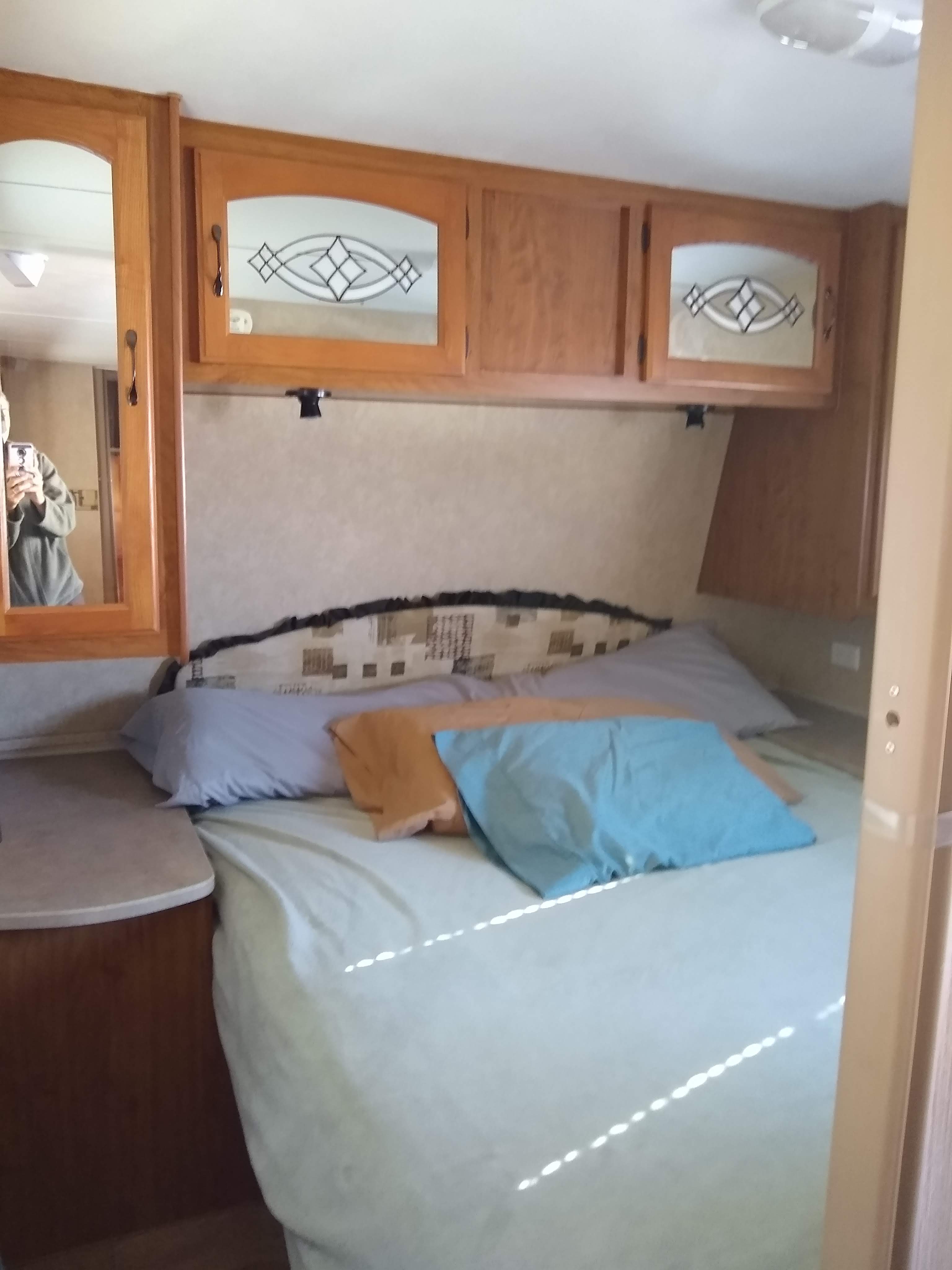 Explore a comfortable RV rental bedroom, featuring wooden cabinets above a compact bed with various pillows.. Frontier Hyperlite 28RBH 2008