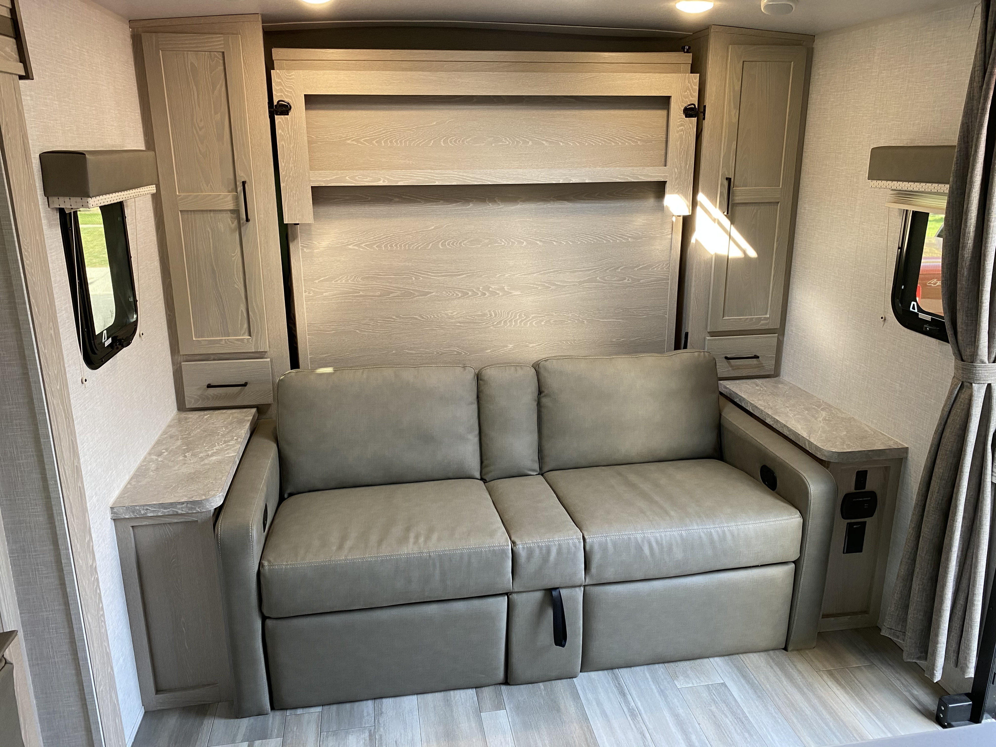Spacious RV rental interior with a light grey sofa and built-in murphy bed, surrounded by light wood cabinetry. Perfect for travel.. Forest River Mini-Lite 2021
