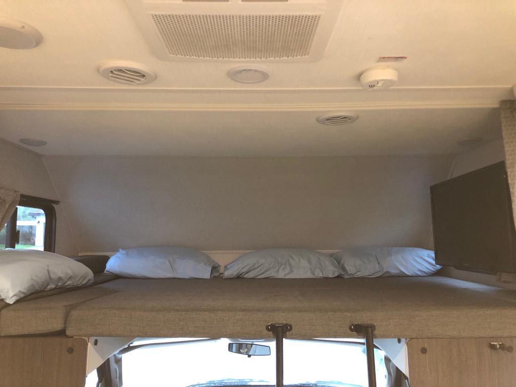 Cozy overhead bunk bed in an RV rental, featuring soft pillows, a TV, and AC vents. Perfect for a comfortable night's sleep.. Forest River sunseeker LE 2350 2020