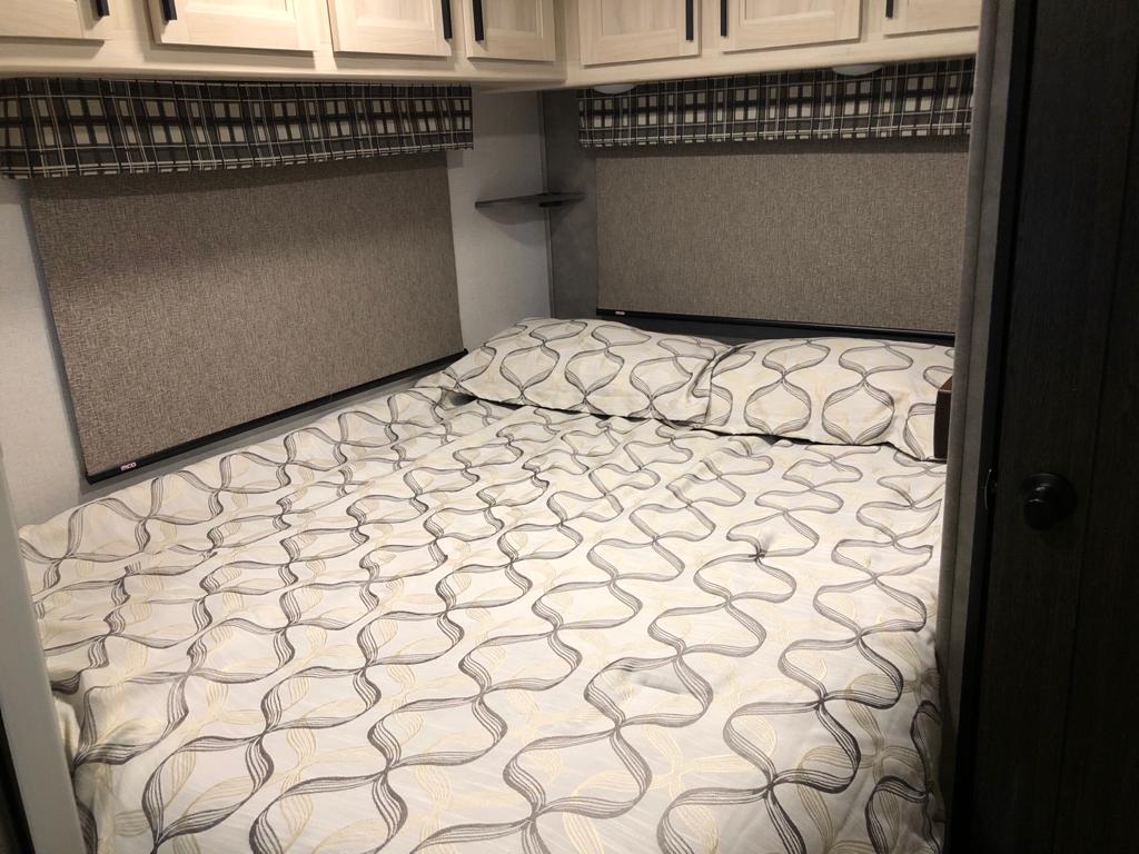 Relax in this RV rental bedroom: a comfy bed, patterned linens, pillows, and functional overhead cabinets.. Forest River sunseeker LE 2350 2020