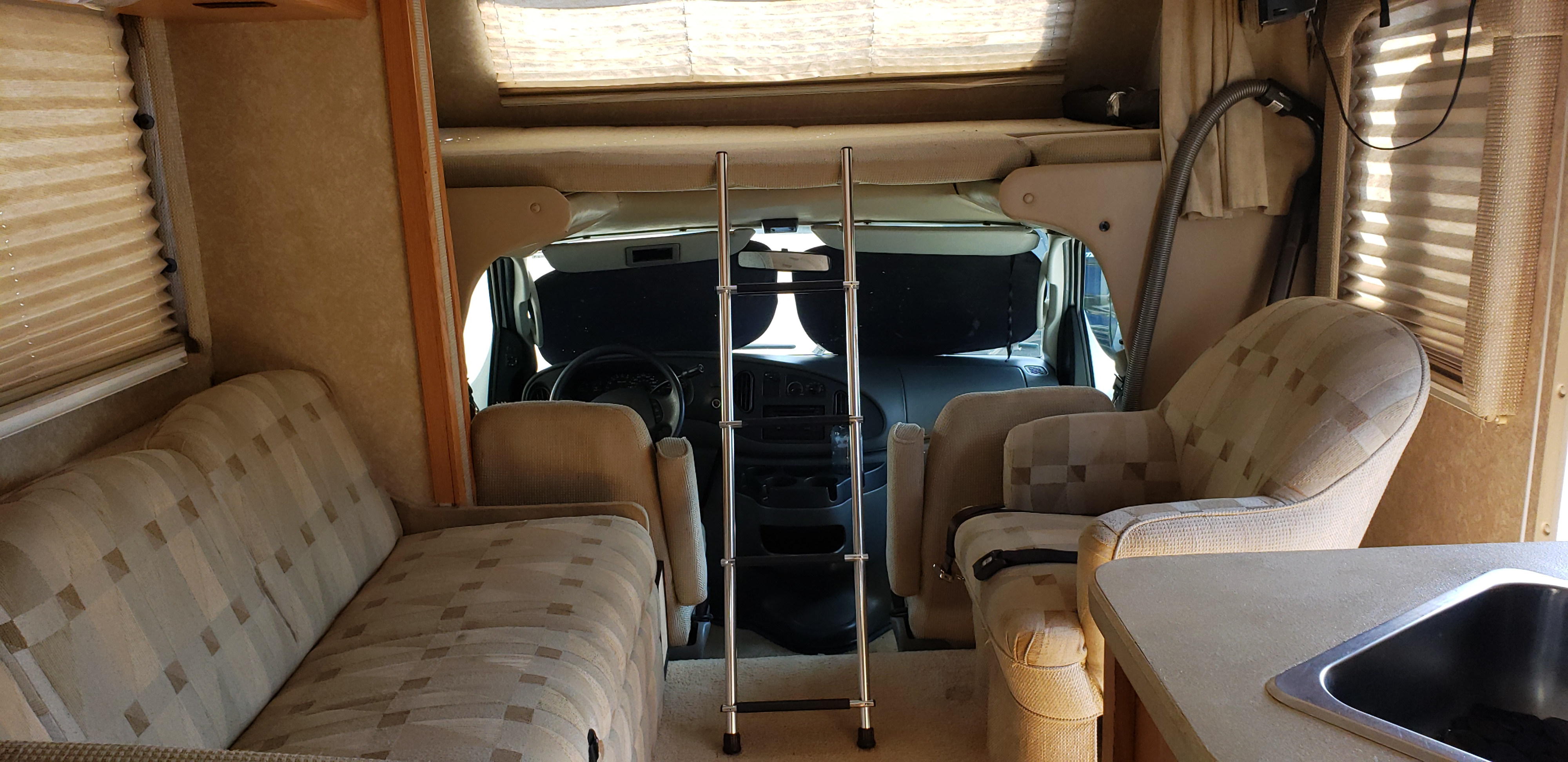 Interior view of an RV rental, showing the living area with sofa, swivel chair, bunk ladder, and partial kitchen sink.. FourWinds P-31 2007