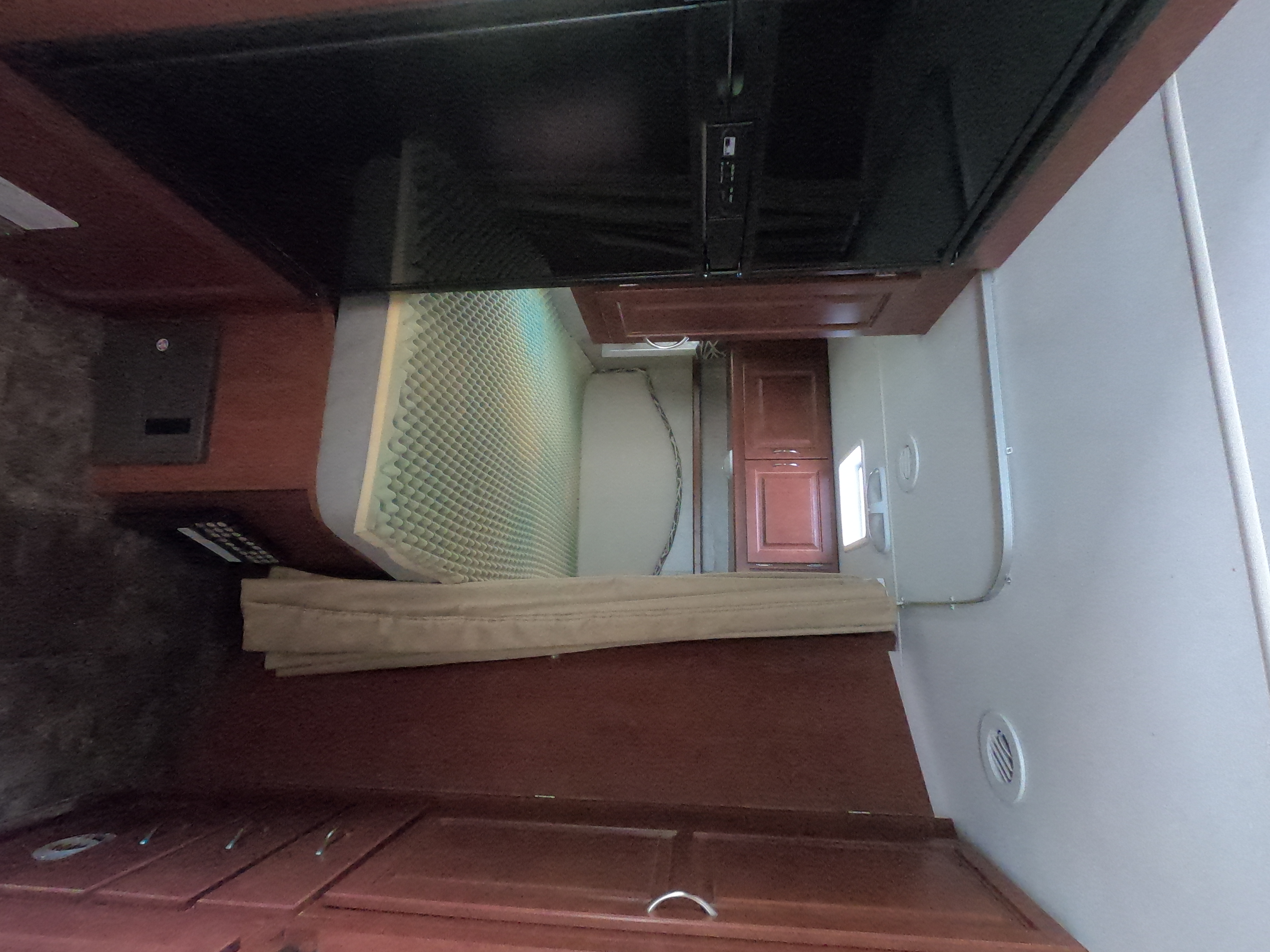 This RV rental interior features a compact sleeping area with a textured mattress topper, mounted TV, and wooden cabinets.. Winnebago Minnie Winnie 2014