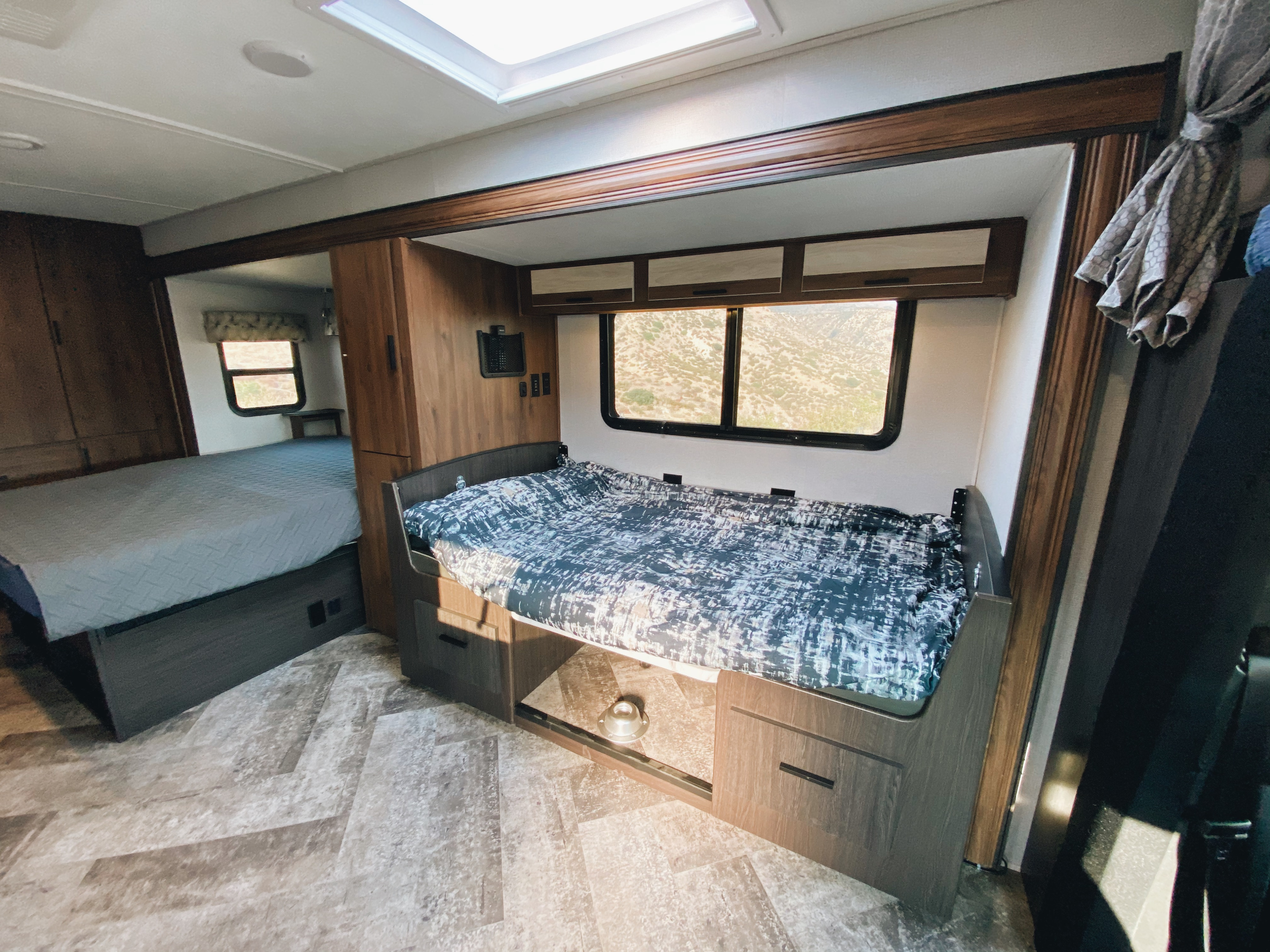 An RV rental's interior shows two beds: a front bunk with patterned bedding & a rear bedroom with a blue quilt.. Forest River Sunseeker 2020