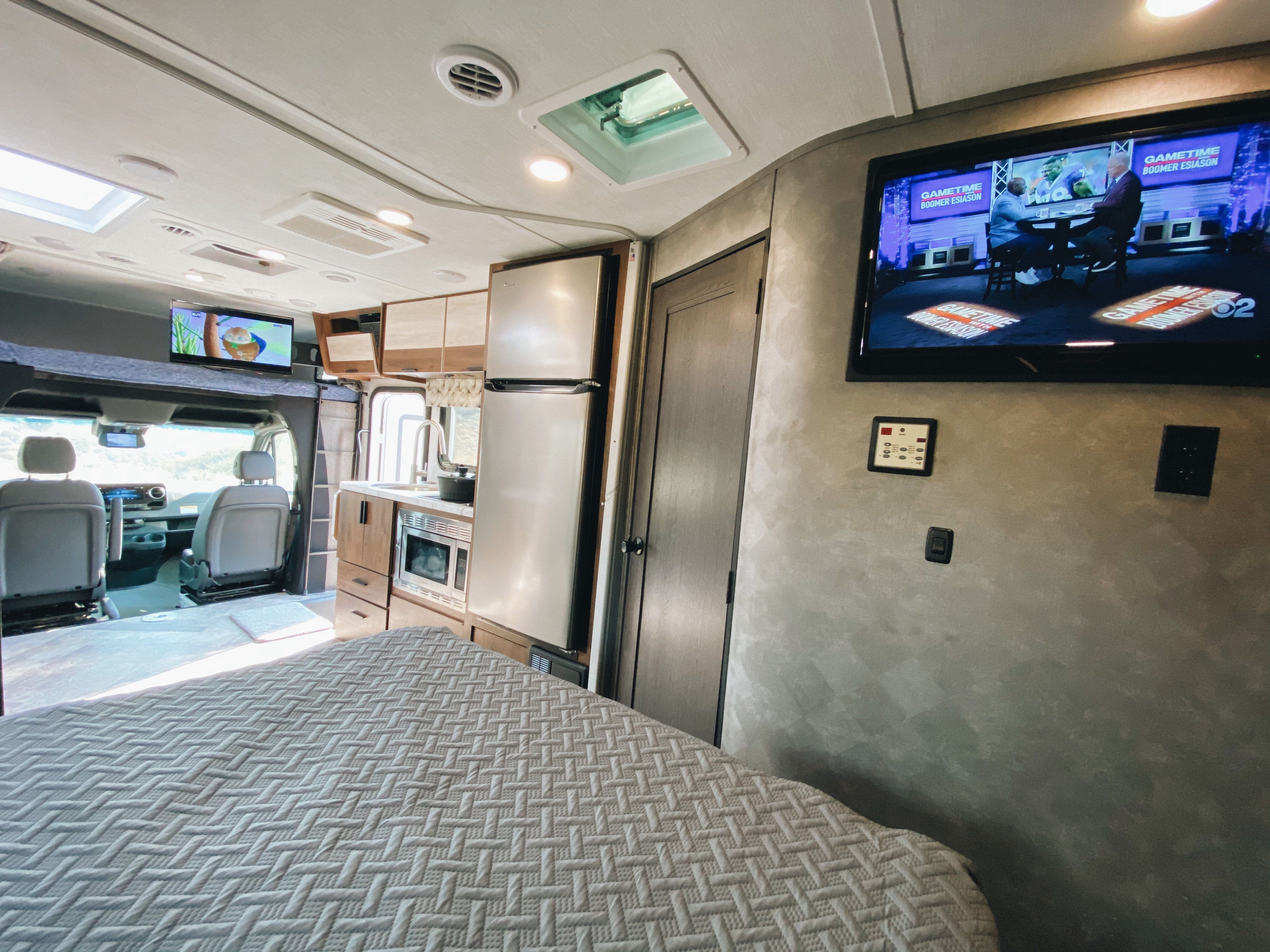 Cozy rv rental interior: main bed, kitchen (fridge, microwave, sink), and driving area. Features multiple TVs and skylights.. Forest River Sunseeker 2020