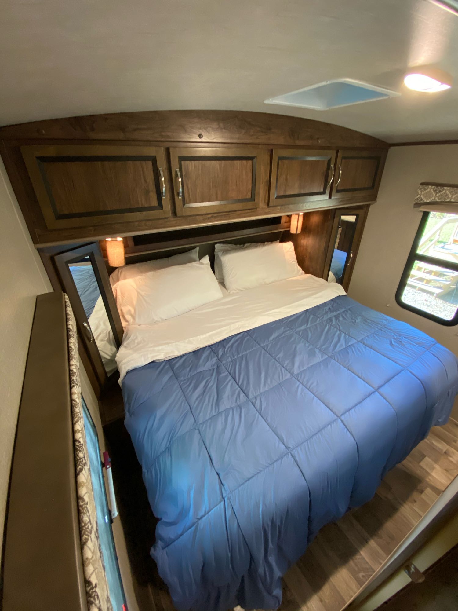 Comfortable RV rental bedroom with a large bed, blue comforter, overhead cabinets, and a window. Ideal for travel.. Other Other 2018