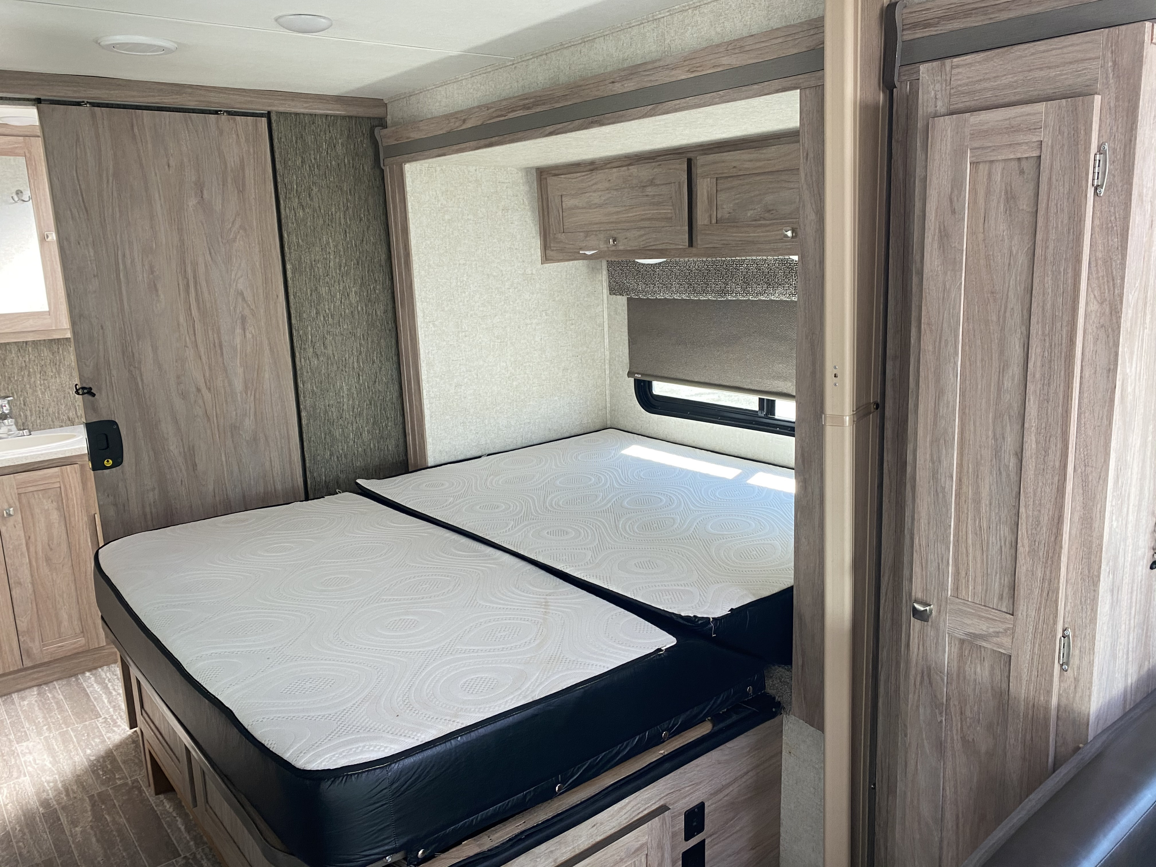 This RV rental interior showcases a cozy bedroom with two comfortable mattresses, overhead cabinets, and an adjacent sink/bathroom area.. Ford E450 2013