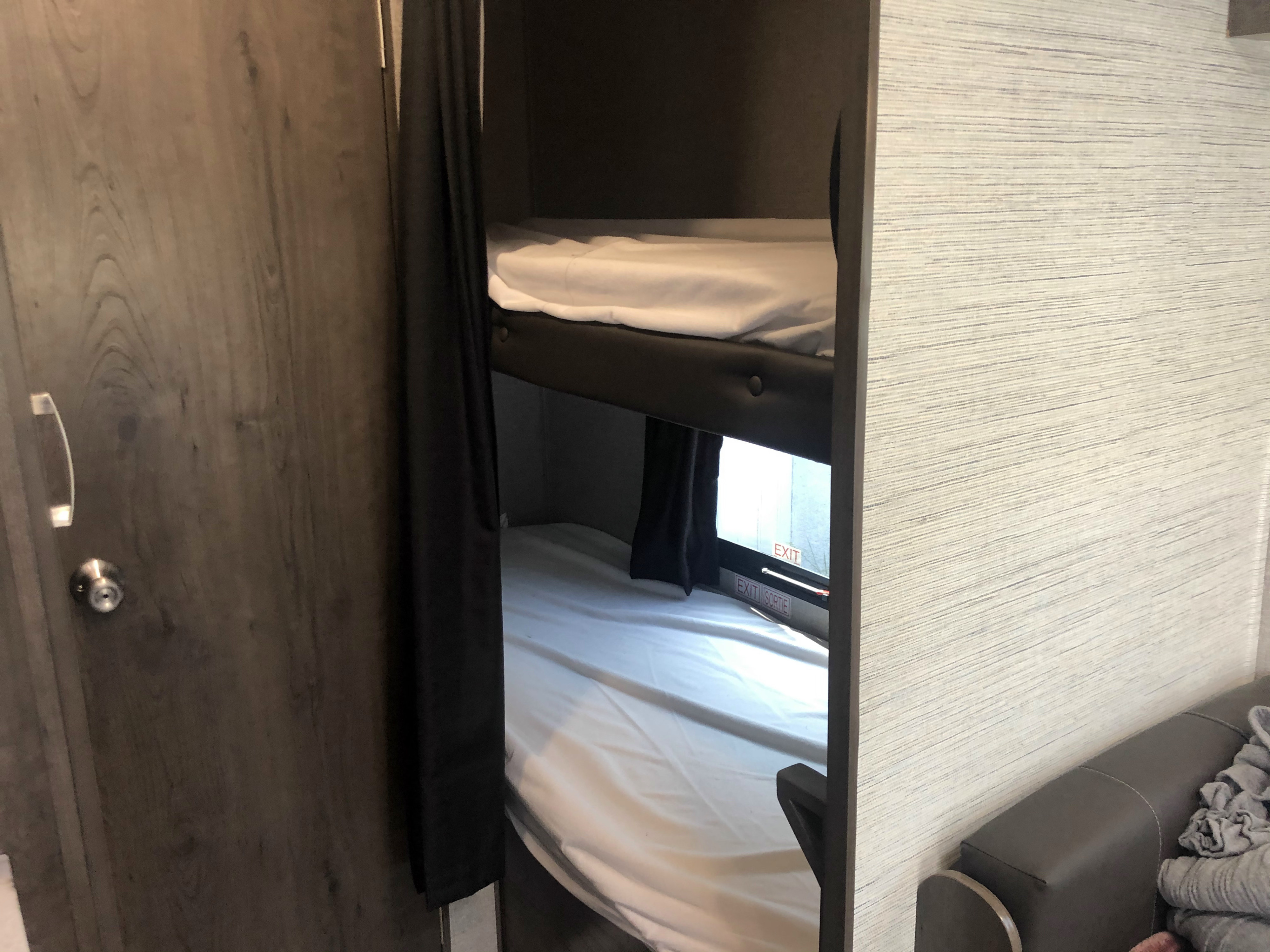 RV rental interior showcasing bunk beds with white linens and an emergency exit window, a cozy sleeping space.. Jayco Jay Flight 2021