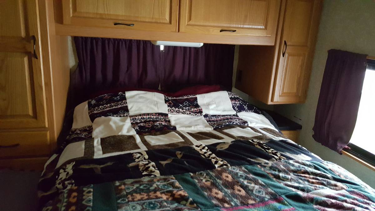 An RV rental's cozy bedroom, showcasing a patterned quilt, wooden overhead storage, and a side window.. Ford Majestic 2007