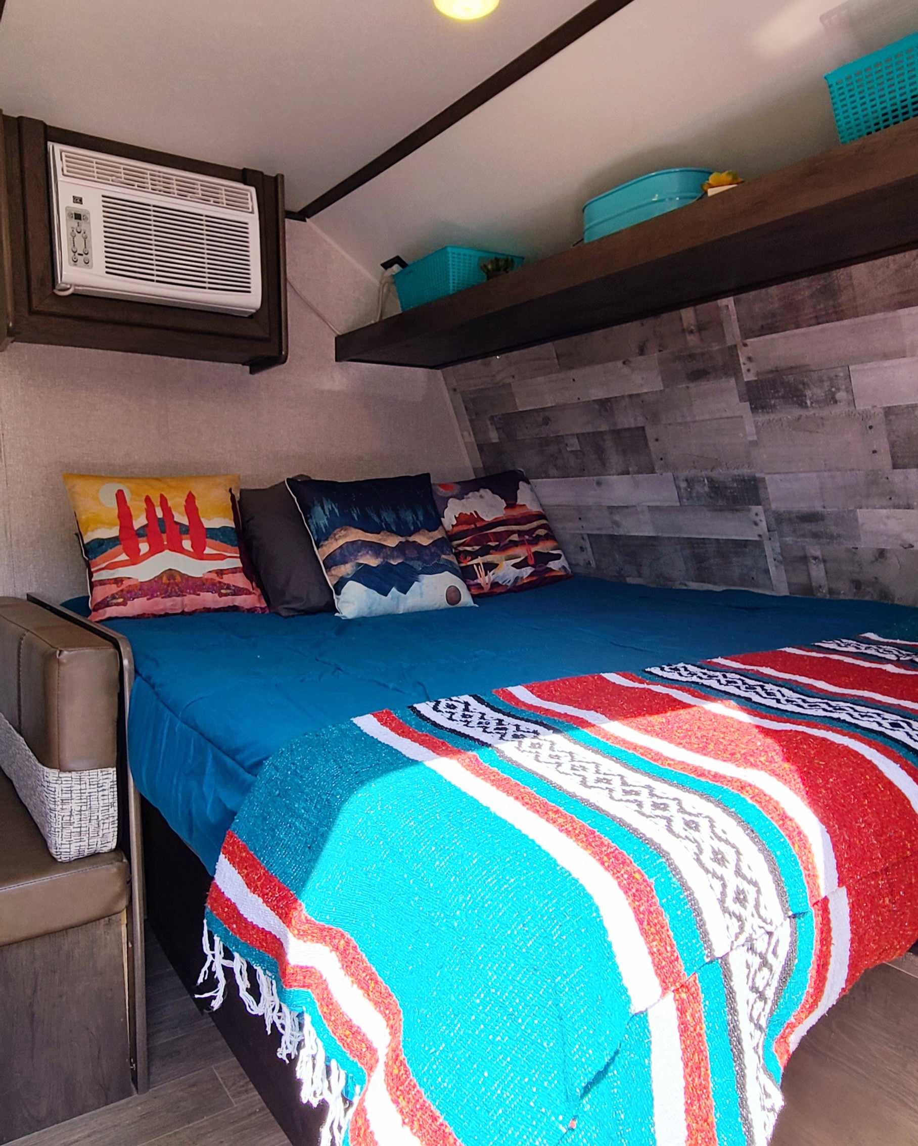 RV rental interior: A cozy bedroom with a bright blue bed, colorful patterned blanket, decorative pillows, and AC unit.. Dutchmen Coleman Lantern LT 2020