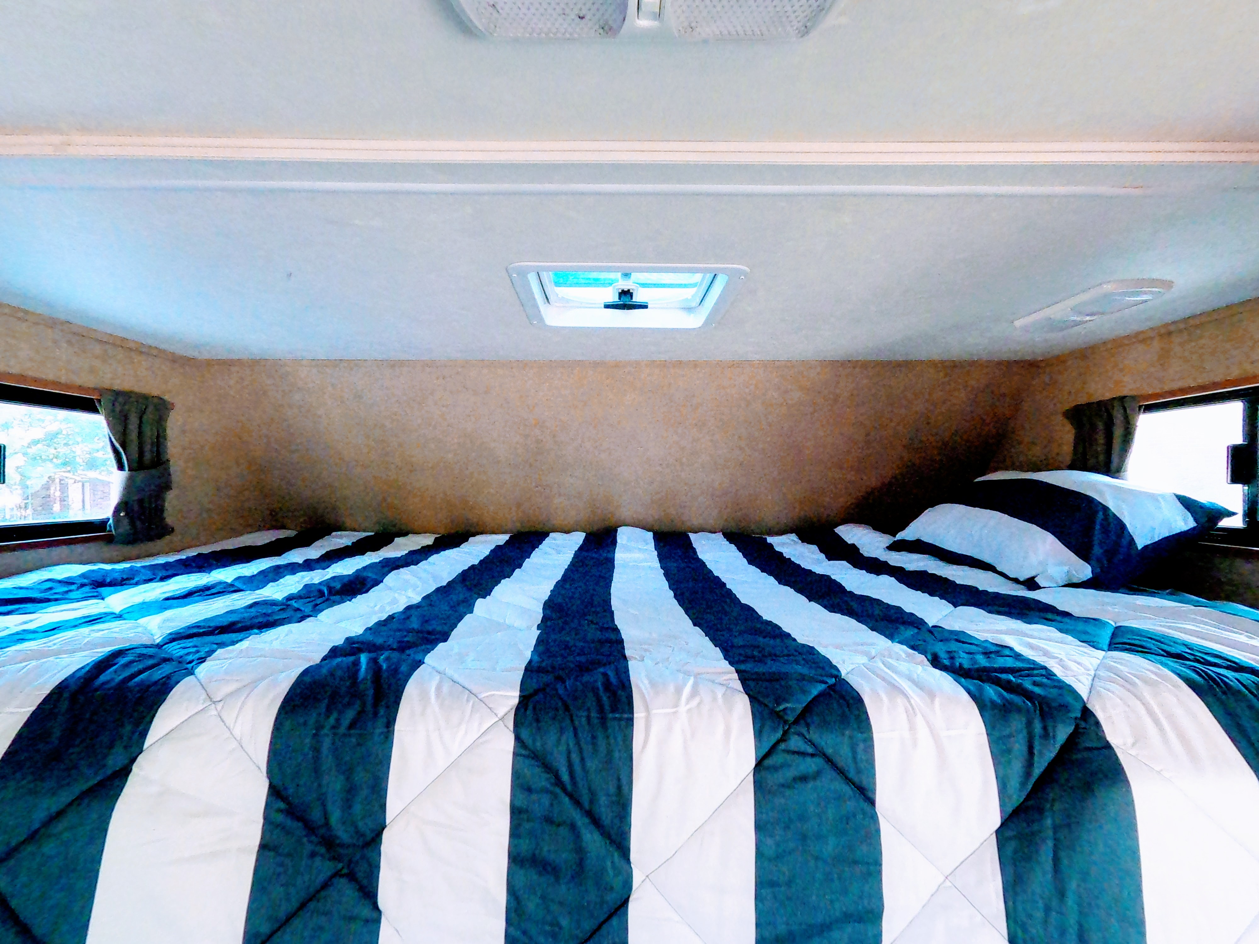 Cozy RV rental bedroom featuring a large striped bed, side windows, and overhead vent.. Other Other 2016