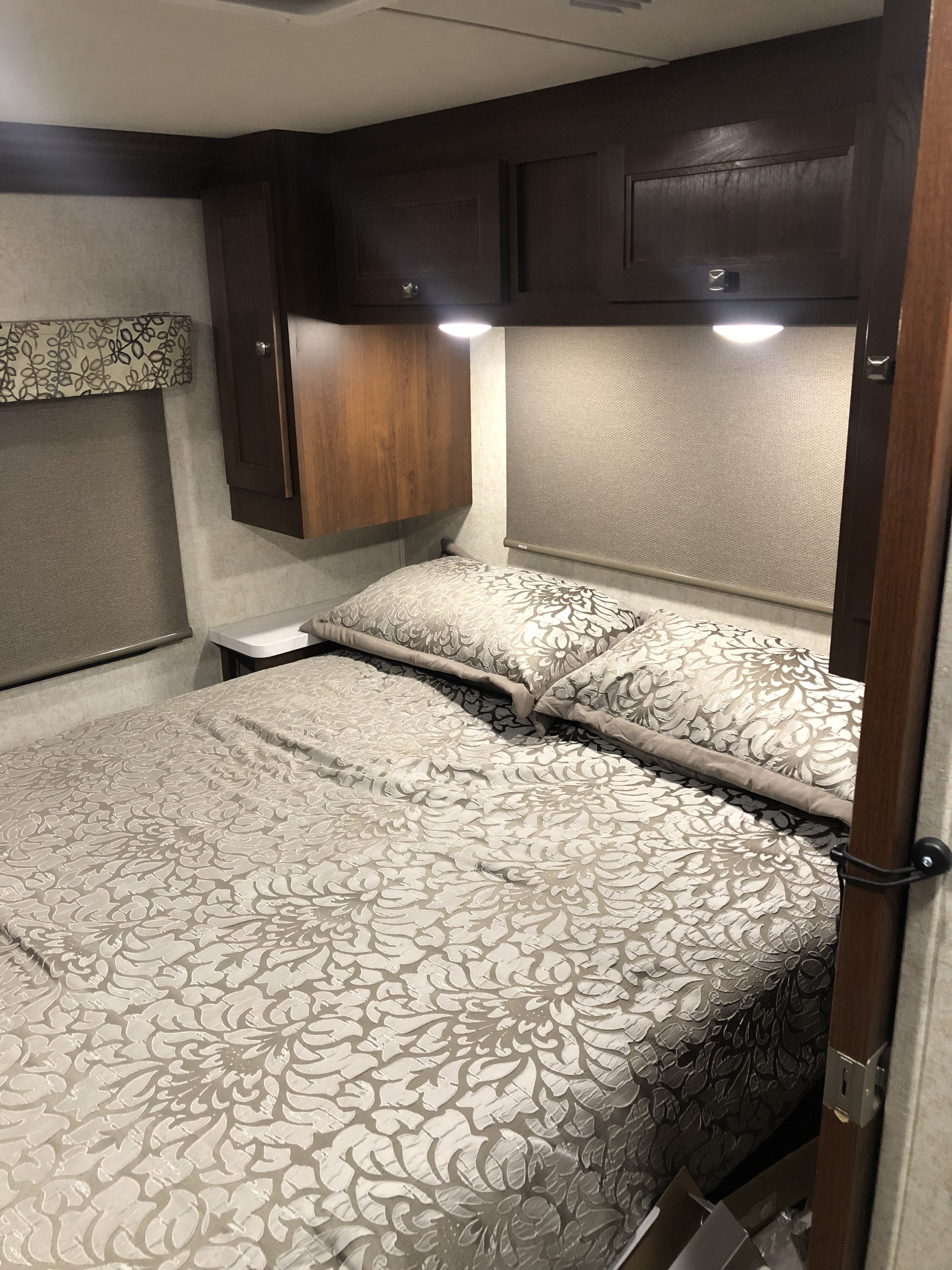 Cozy RV rental bedroom featuring patterned bedding, overhead storage cabinets, and roller blinds for a comfortable stay.. Forest River forester 2019