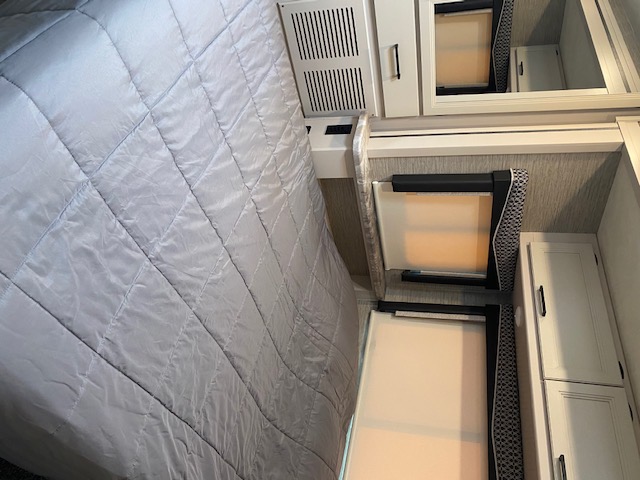 Compact RV rental bedroom with quilted bed, built-in storage, mirror, and blinds. Ideal for travel.. Thor Motor Coach Chateau 2021