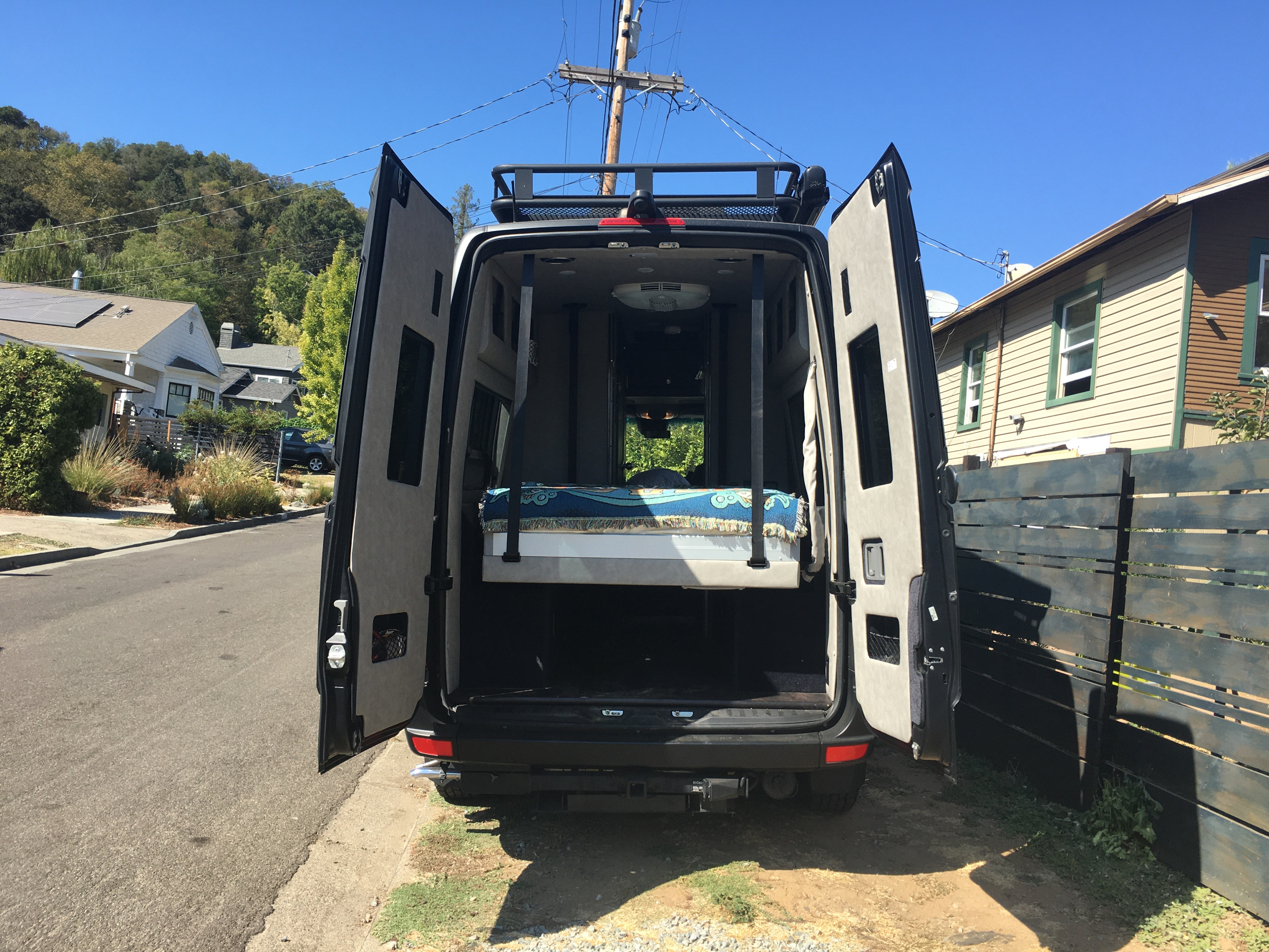 Rear view of an RV rental with open doors, showing a comfortable raised bed and ample storage. Ready for adventure!. Mercedes-Benz Sprinter 2018