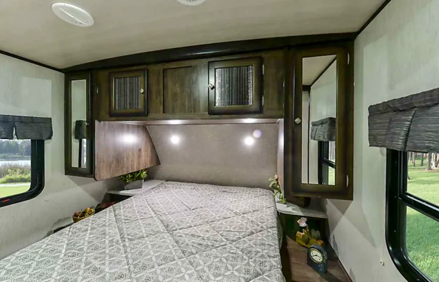 Cozy RV rental bedroom featuring a patterned comforter, overhead storage cabinets, and scenic window views. Ideal for travel.. Heartland Mallard 2019