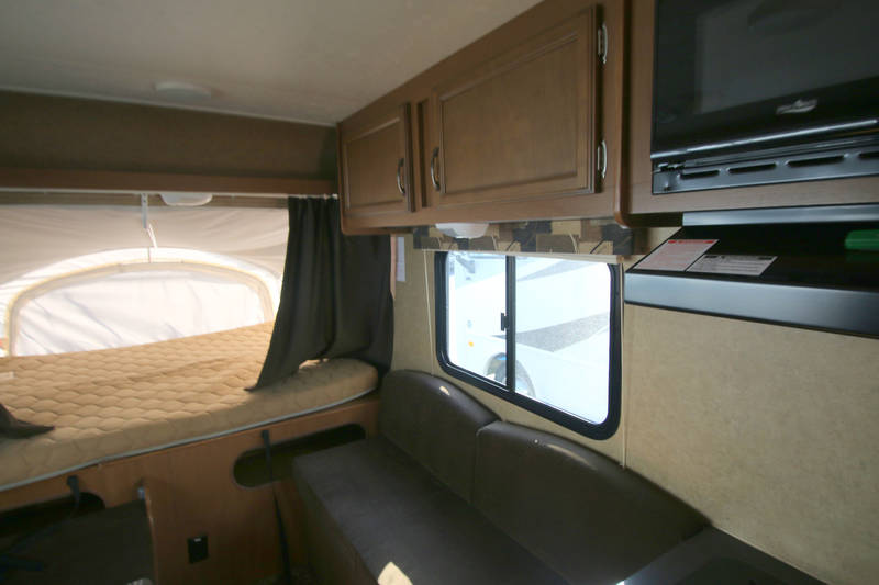An RV rental interior with a cozy pop-out bed on the left, a sofa on the right, and overhead cabinets.. Starcraft Launch 2014