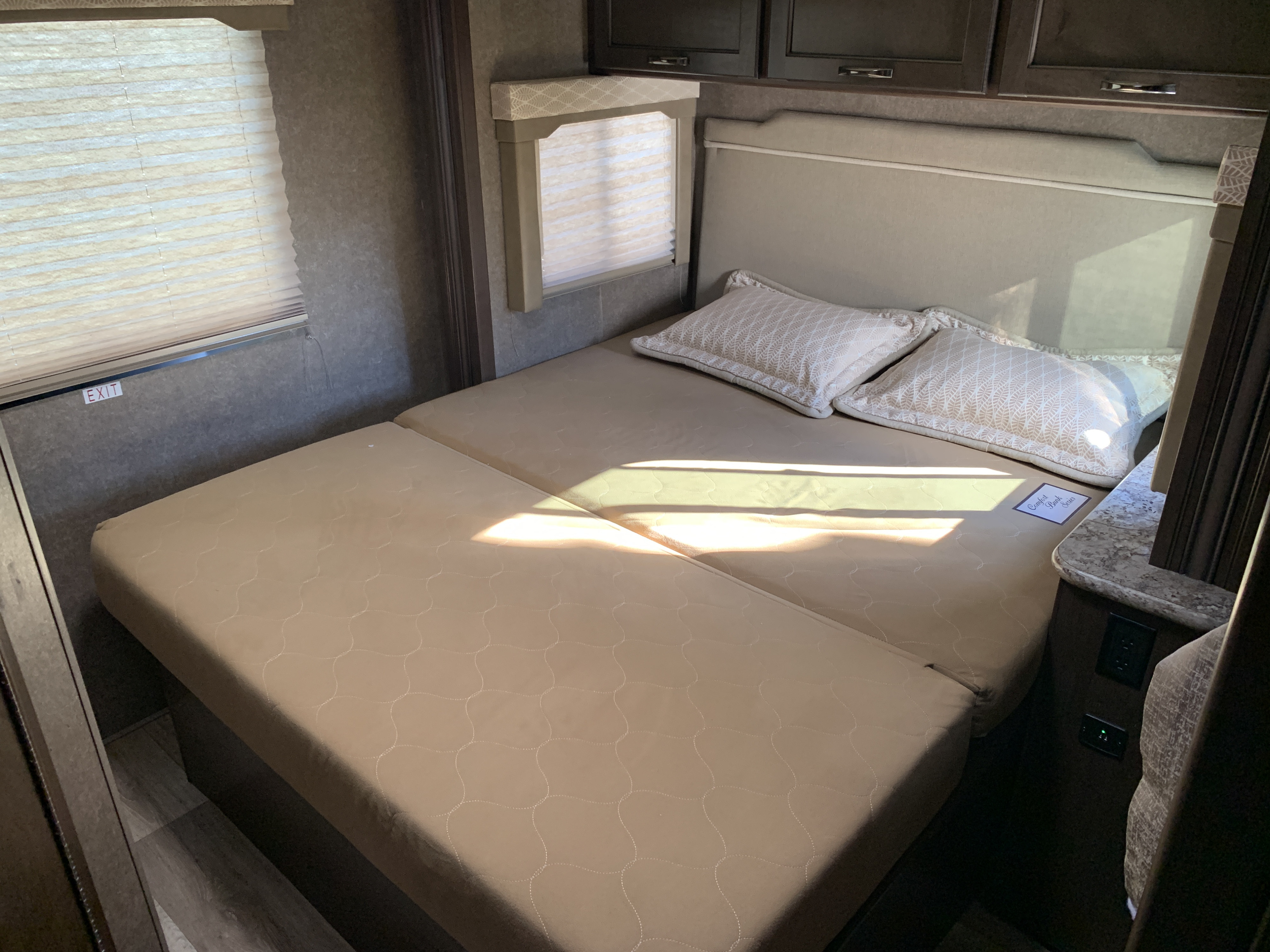 This cozy RV rental features a multi-section bed with decorative pillows, overhead cabinets, and window blinds.. Thor Freedom Elite 2021