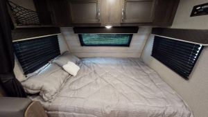 This RV rental bedroom features a comfy queen bed with grey bedding, overhead storage, and privacy blinds for travel.. Jayco 184BS 2021