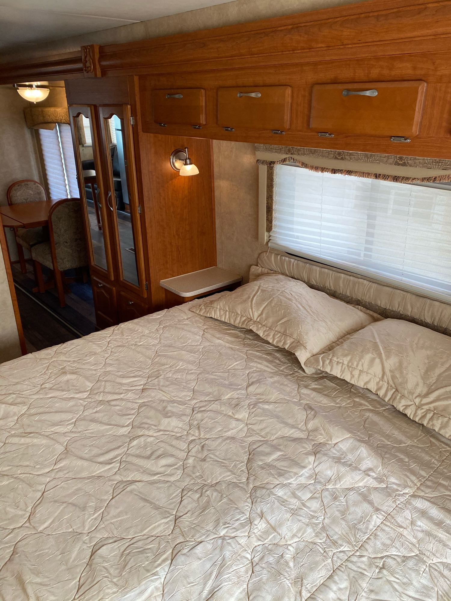 Inside an RV rental: a bright bedroom with a queen bed, wooden cabinets, and a mirrored closet. Dining area seen beyond.. Georgetown XL 2008