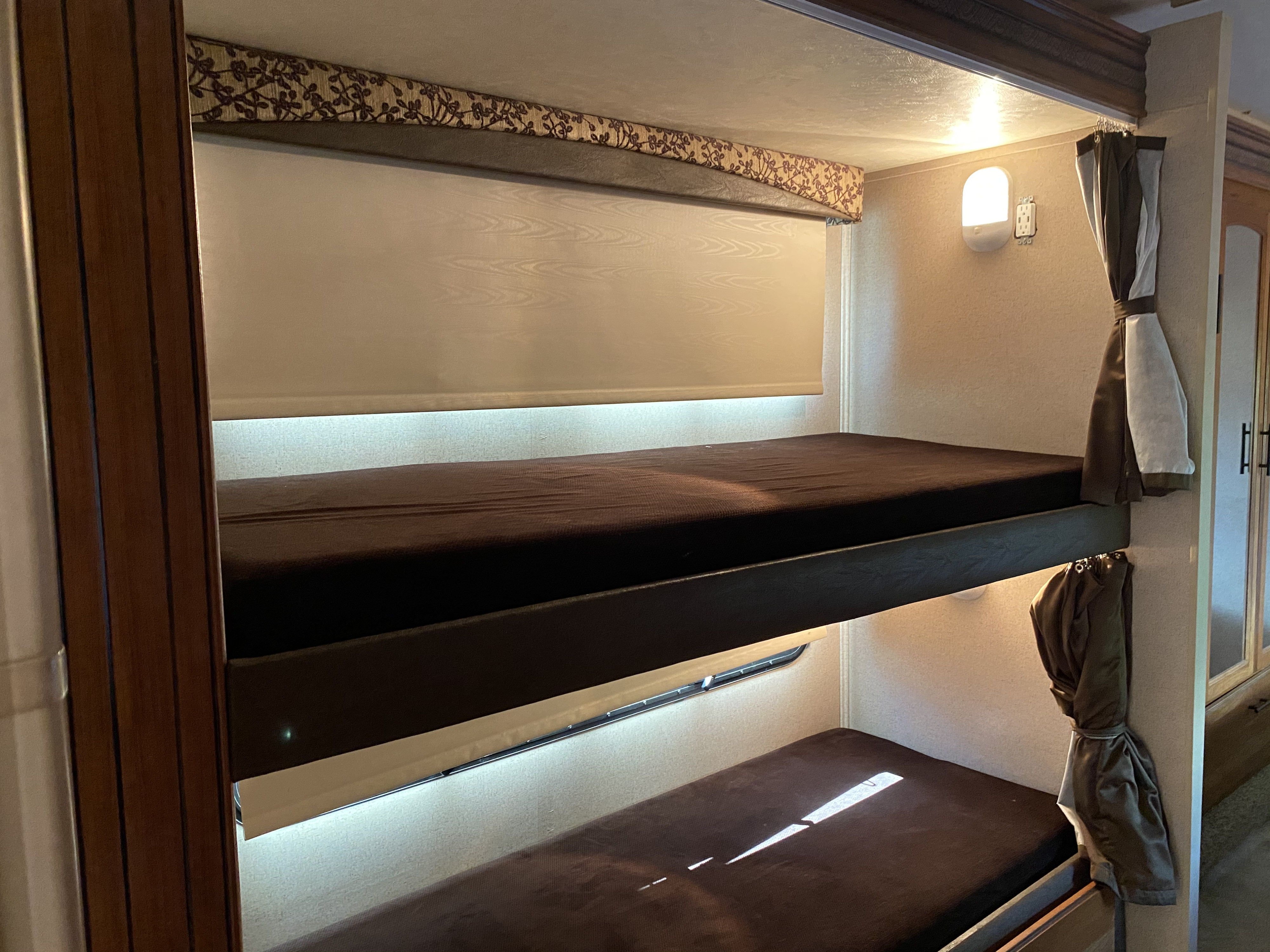 Inside an rv rental: Cozy stacked bunk beds with a brown mattress, built-in lighting, and window shade for comfort.. Jayco Redhawk 2017