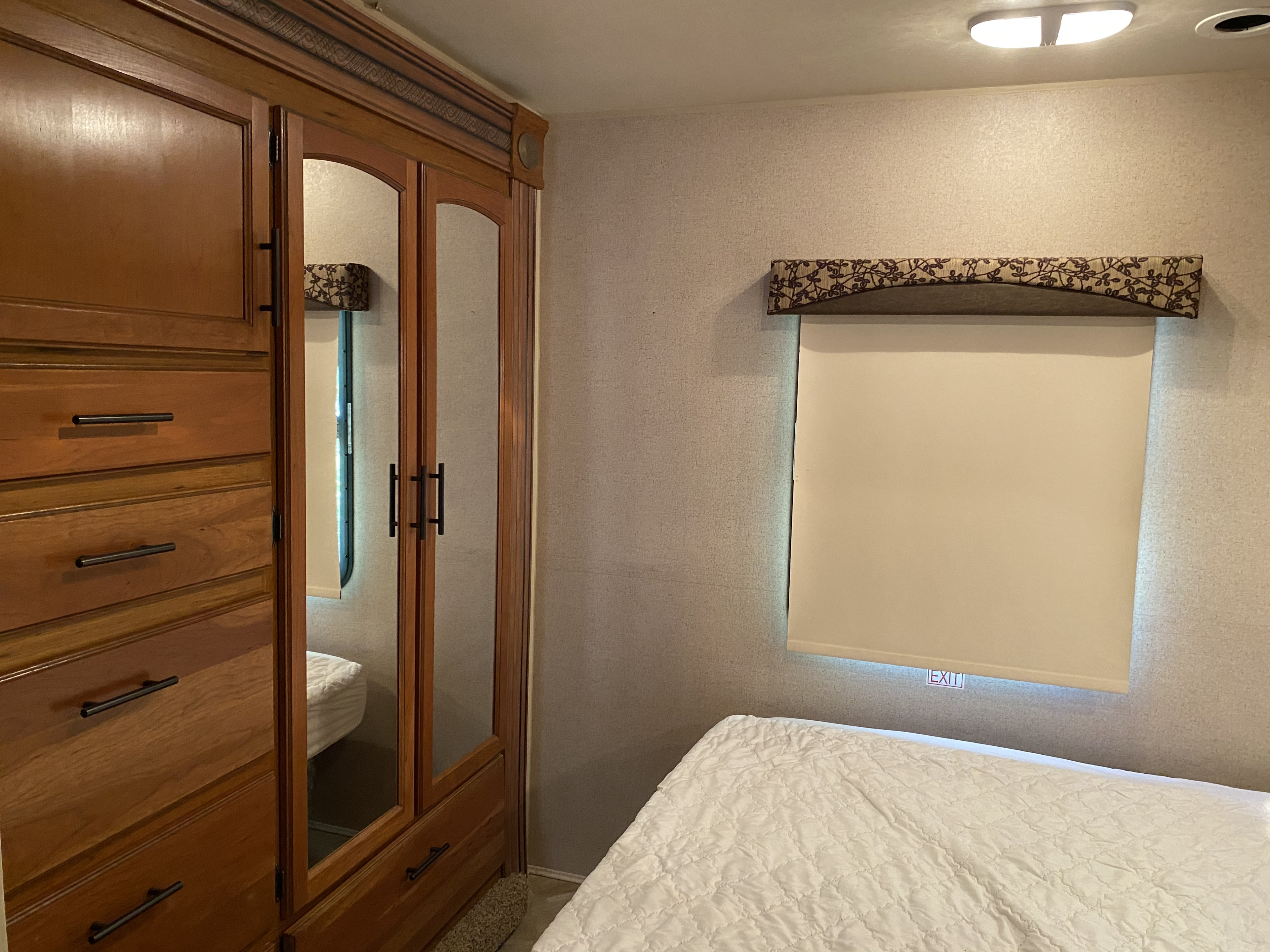 RV rental bedroom showing a wooden wardrobe, mirrored doors, bed, and window with an 'EXIT' sign.. Jayco Redhawk 2017