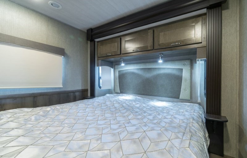 Step into comfort with this RV rental bedroom, showcasing a stylish headboard, overhead storage, and patterned bedding.. Nexus Wraith 2021
