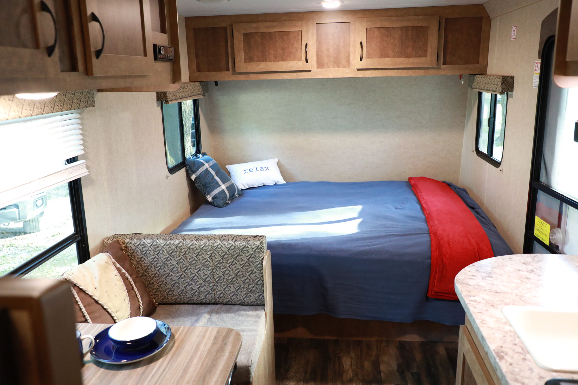 Inside a bright RV rental: a comfortable bed with 'relax' pillow, dinette, compact kitchen, and overhead cabinets.. Starcraft Launch 2017