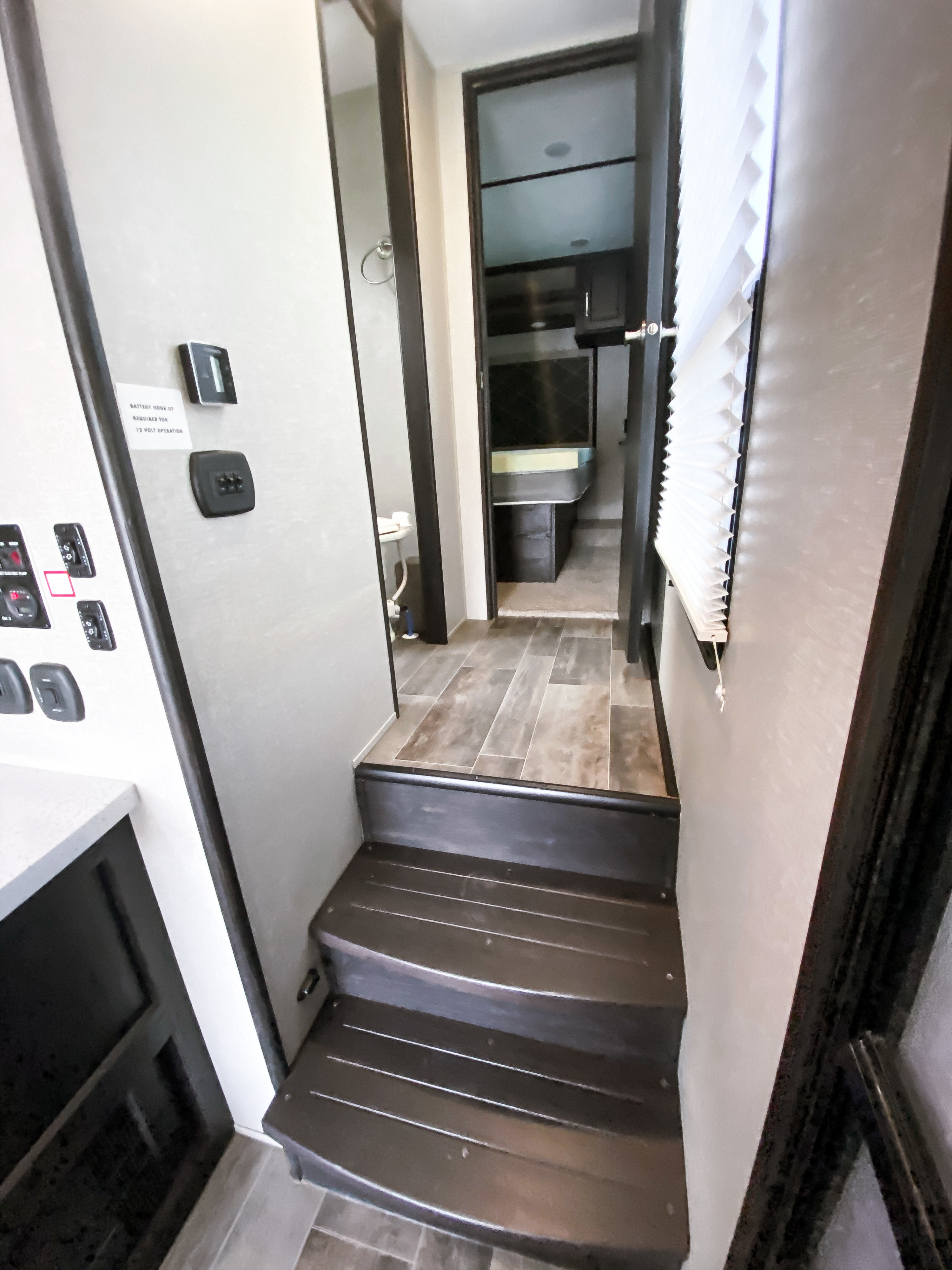RV rental interior: steps lead to hallway with bathroom & bedroom access. Control panel and window blinds shown.. Keystone Impact 2018