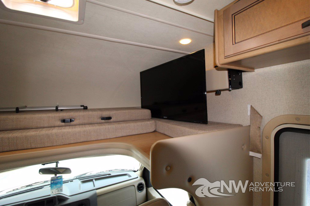 Inside an RV rental: a cozy cabover bunk with cushions and a mounted TV, ready for relaxation on your trip.. Thor Motor Coach Four Winds 2020