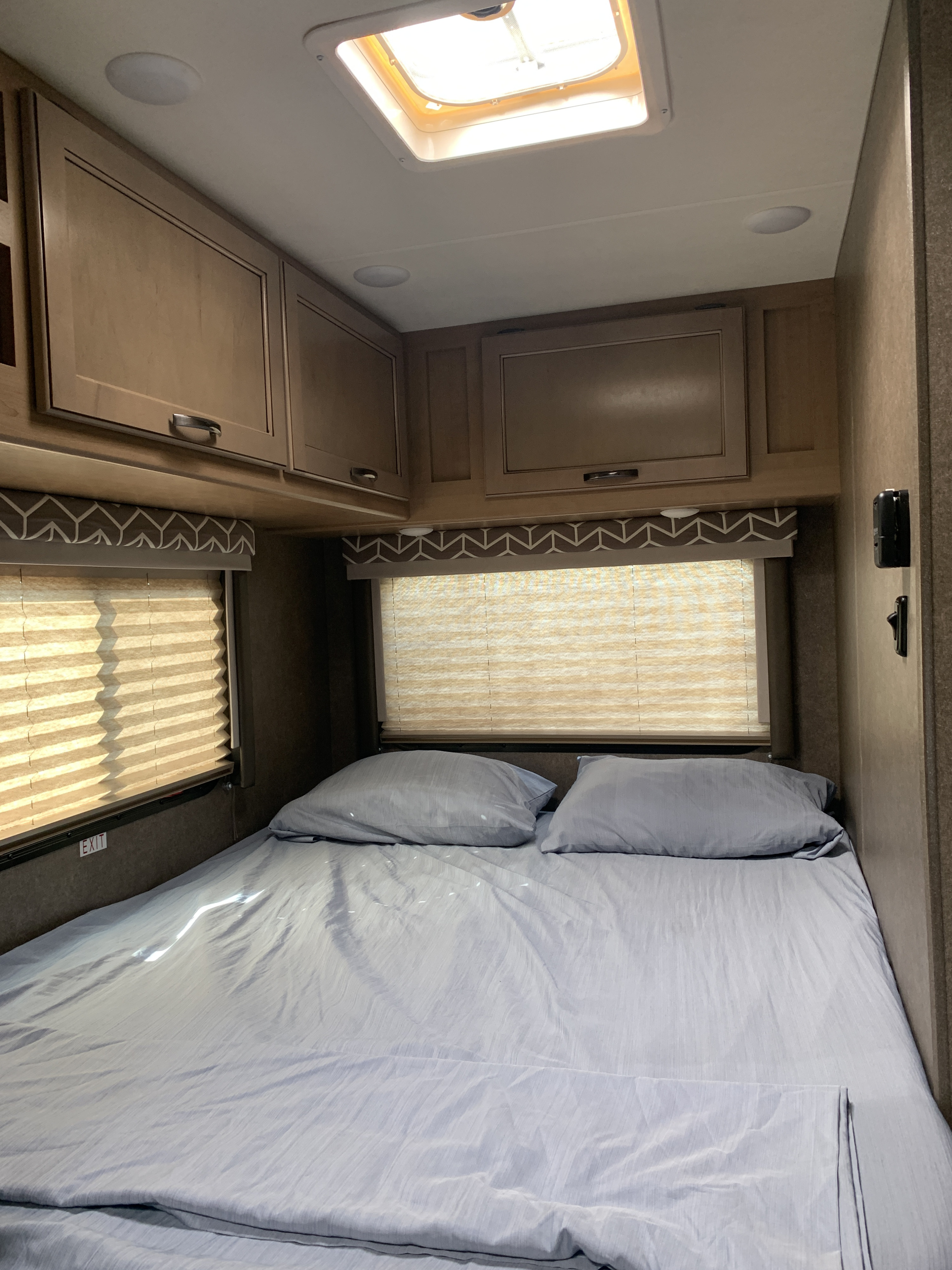 RV rental bedroom: cozy sleeping area with light blue bedding, overhead cabinets, and windows with blinds.. Thor Daybreak 2020