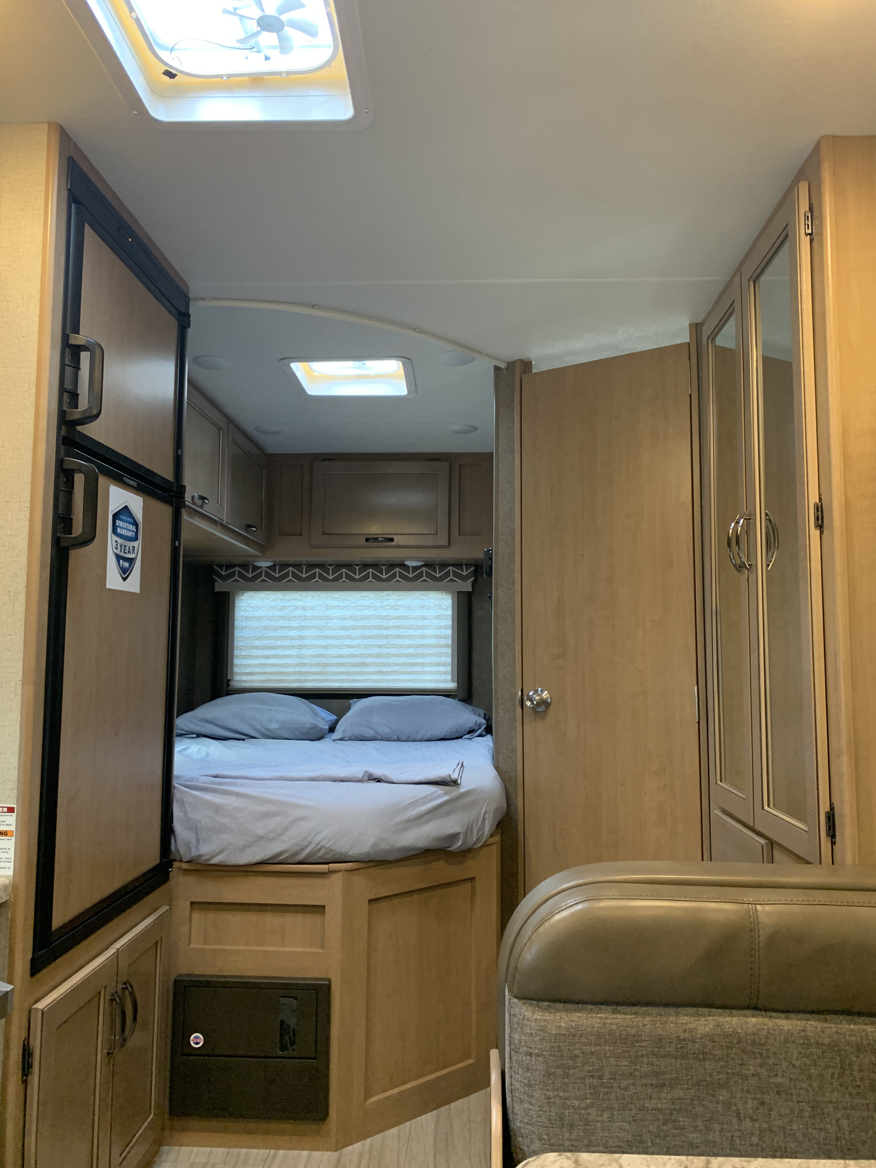 Cozy RV rental interior featuring a light blue bed, refrigerator, and wooden cabinetry with a ceiling vent.. Thor Daybreak 2020