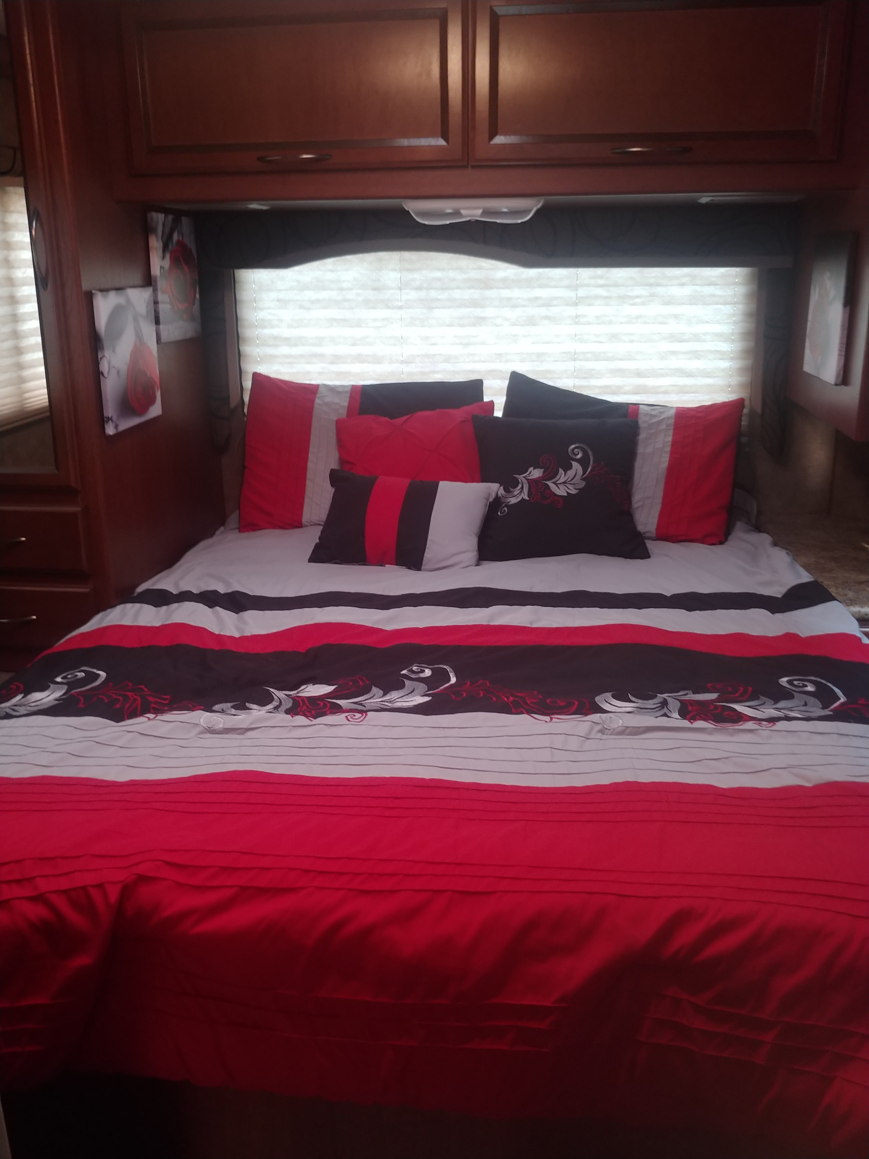 Stylish red, black, and white bedding in a comfy RV rental bedroom, with overhead storage.. Thor Motor Coach Freedom Elite 2013
