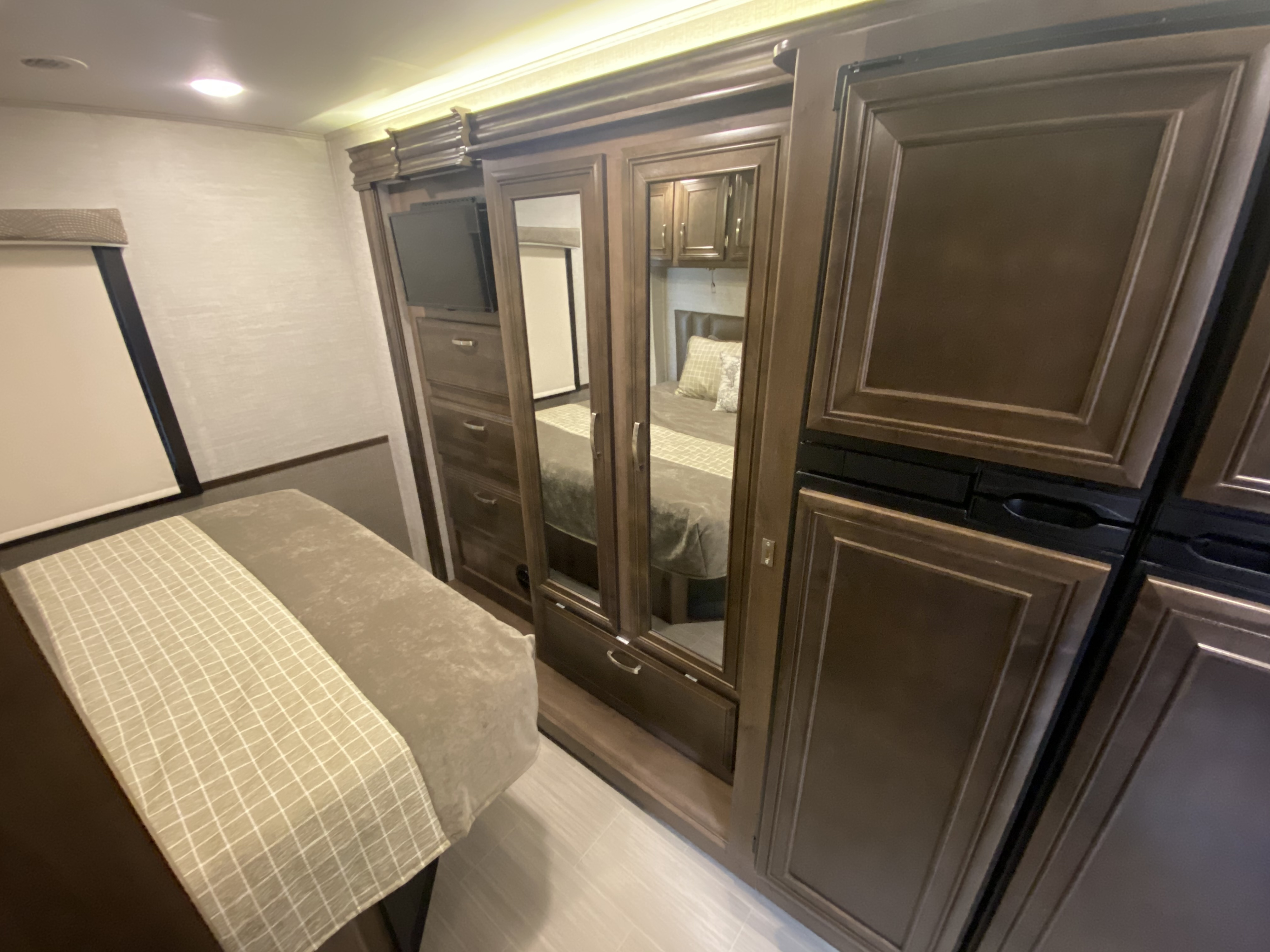RV rental bedroom showing a bed, built-in wardrobe with TV, and integrated refrigerator.. Entegra Coach Other 2021