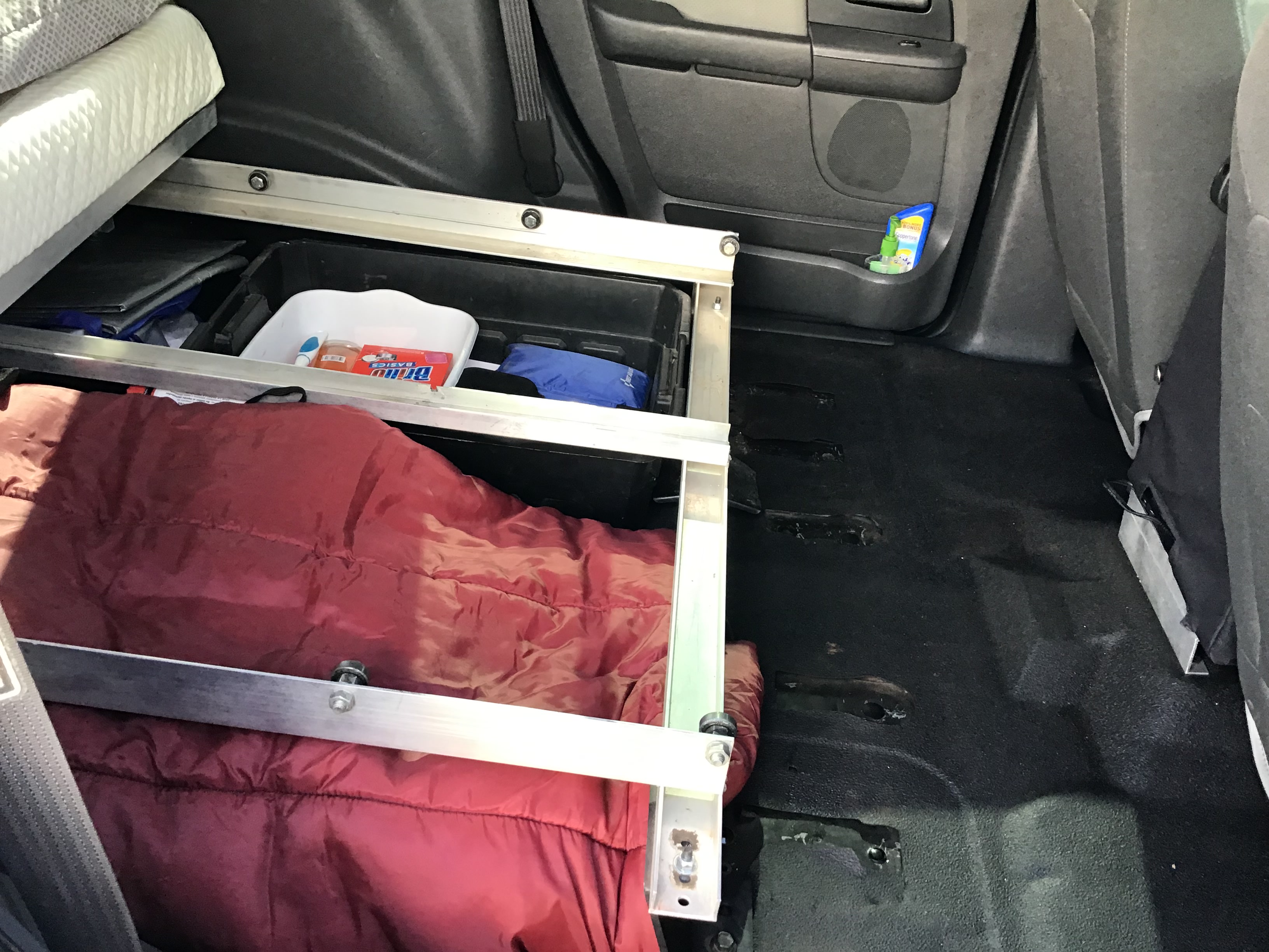 RV rental vehicle interior: organized storage setup with sleeping platform, red sleeping bag, and travel essentials.. Ford Campervan Expedition Adventure 4x4 Camper Van Conversion 2007