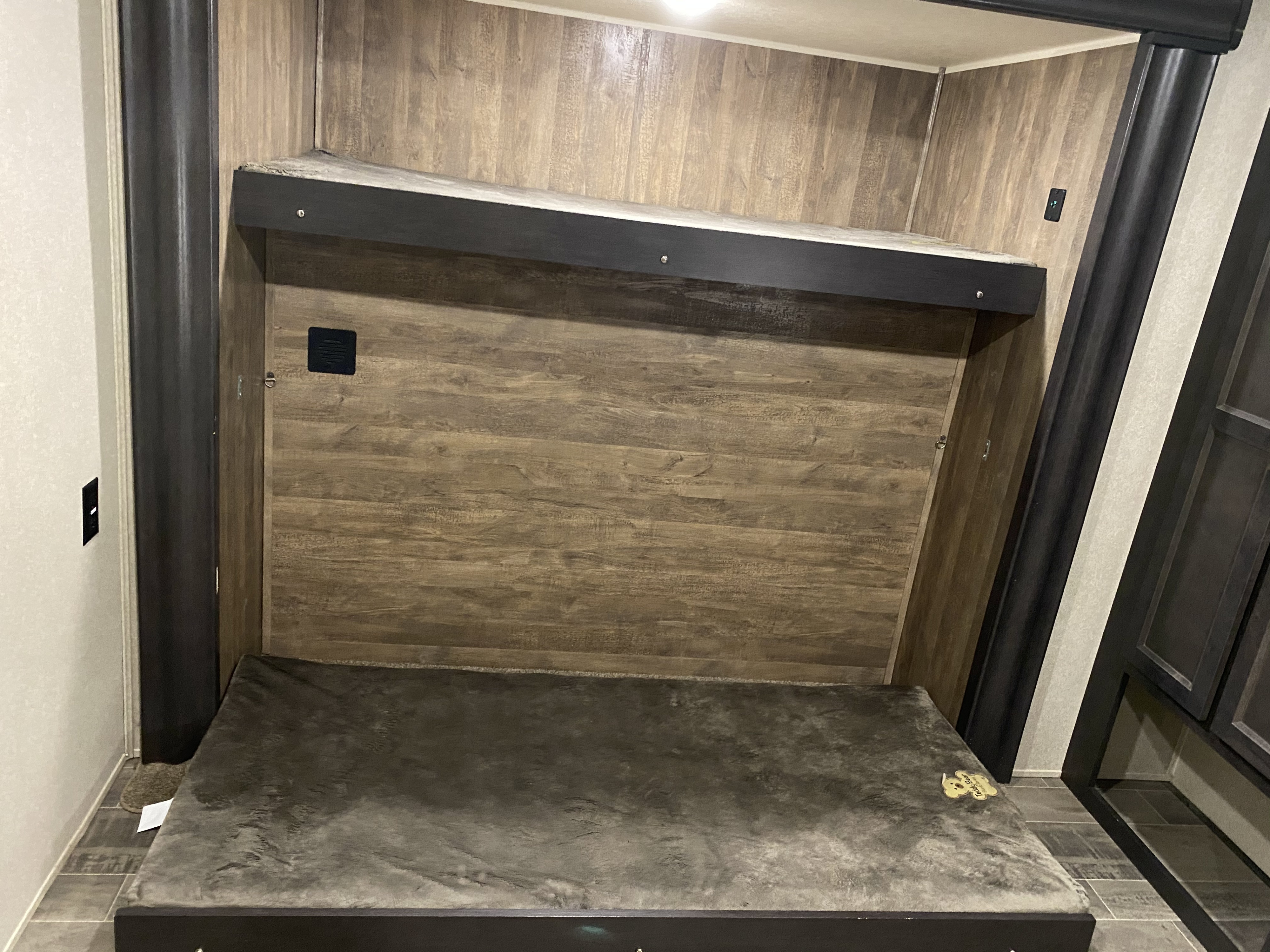 RV rental with clever bunk beds. The top bunk is folded up against the wood-paneled wall, showing the lower bed with a gray mattress.. Palomino Puma 2018