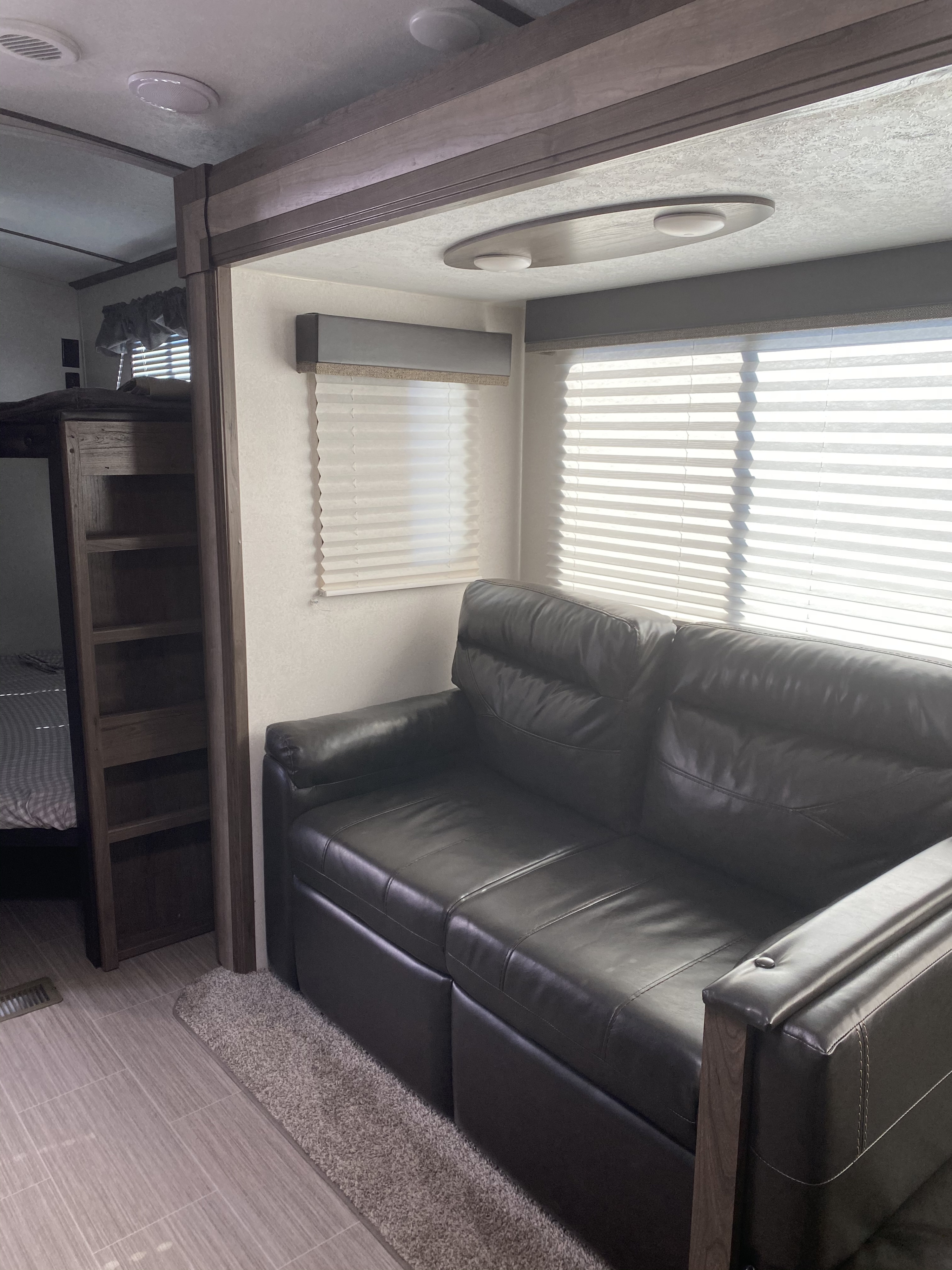Modern RV rental living space with a dark leather sofa, bunk beds, and large windows. Perfect for your next adventure.. Keystone RV Passport GT 2021