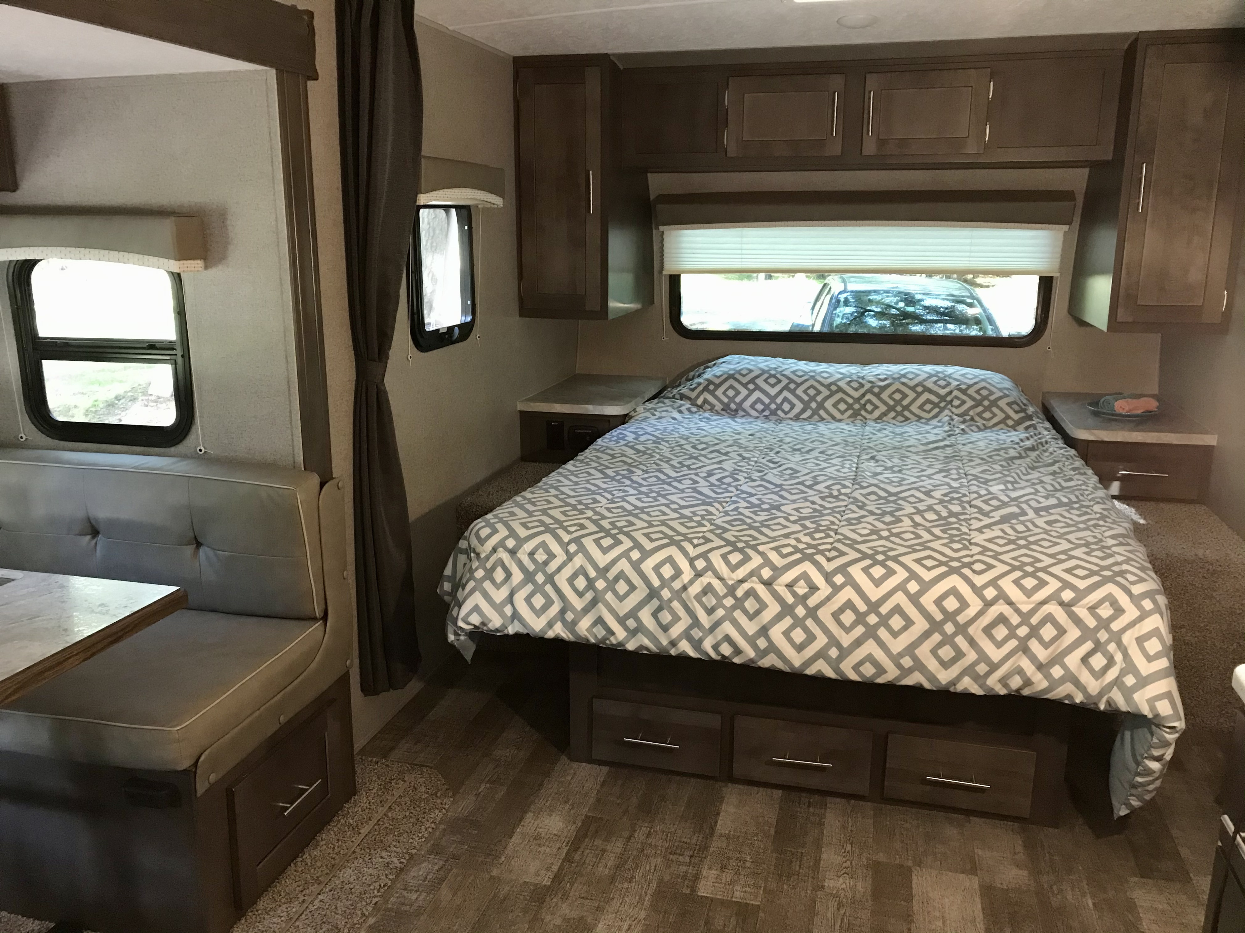 An RV rental's bedroom and dinette area, featuring a patterned comforter, grey seating, and overhead cabinets.. Forest River Mini-Lite 2020