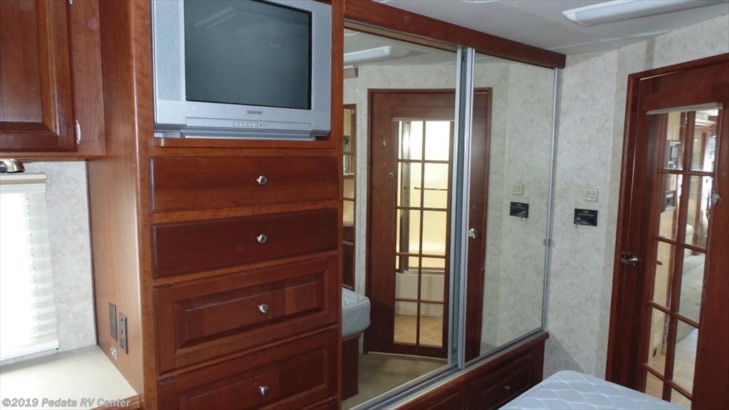RV rental bedroom with TV, wood drawers, and mirrored closet reflecting the bathroom area.. THOR Four Winds Infinity 2005
